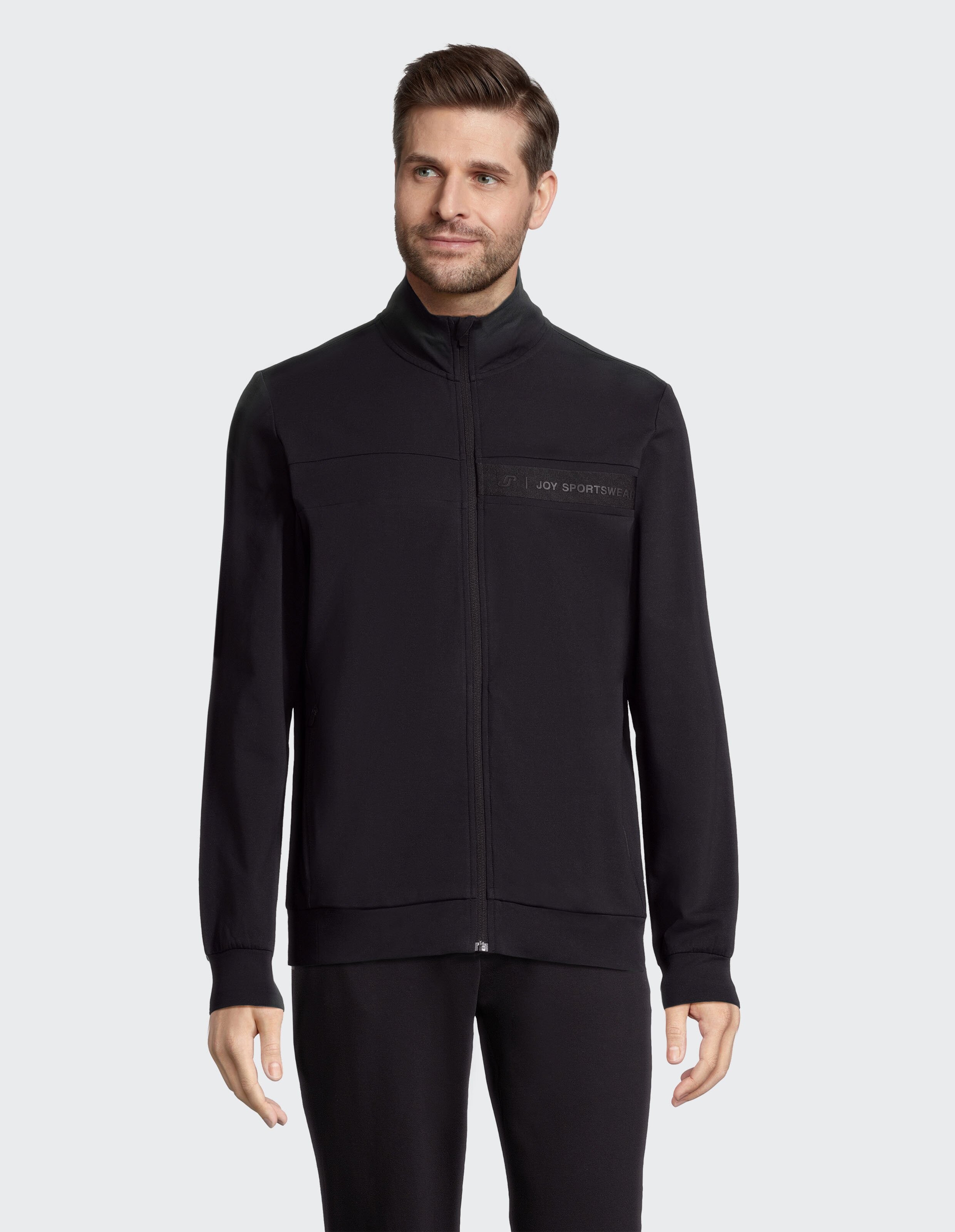 Schwarze Jacke mit hohem Kragen und Reißverschluss; dezentes Logo Joy Sportswear auf der Brust, elastische Bündchen.