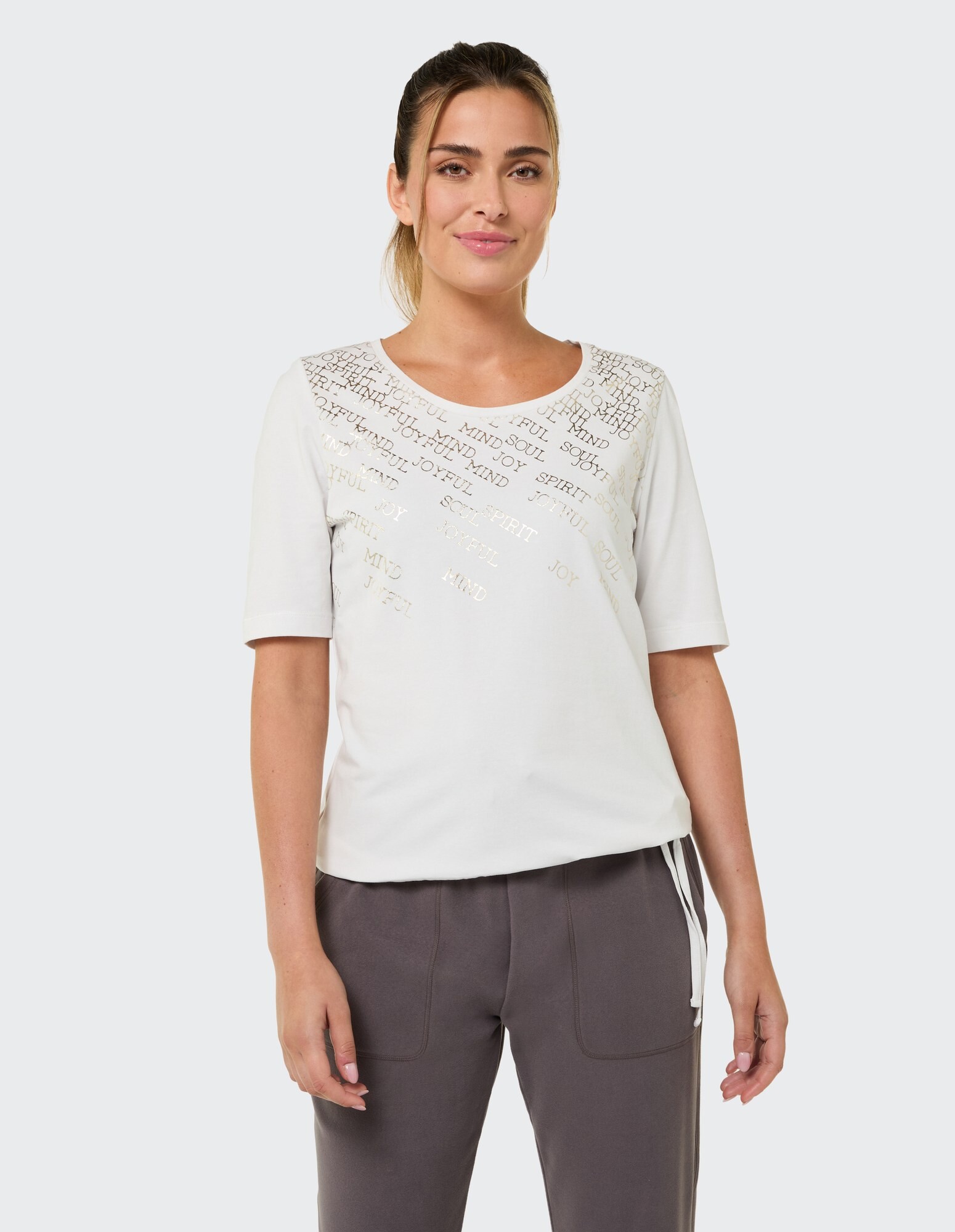 Lässiges weißes T-Shirt mit metallischem Text, gepaart mit einer grauen Lounge-Hose.