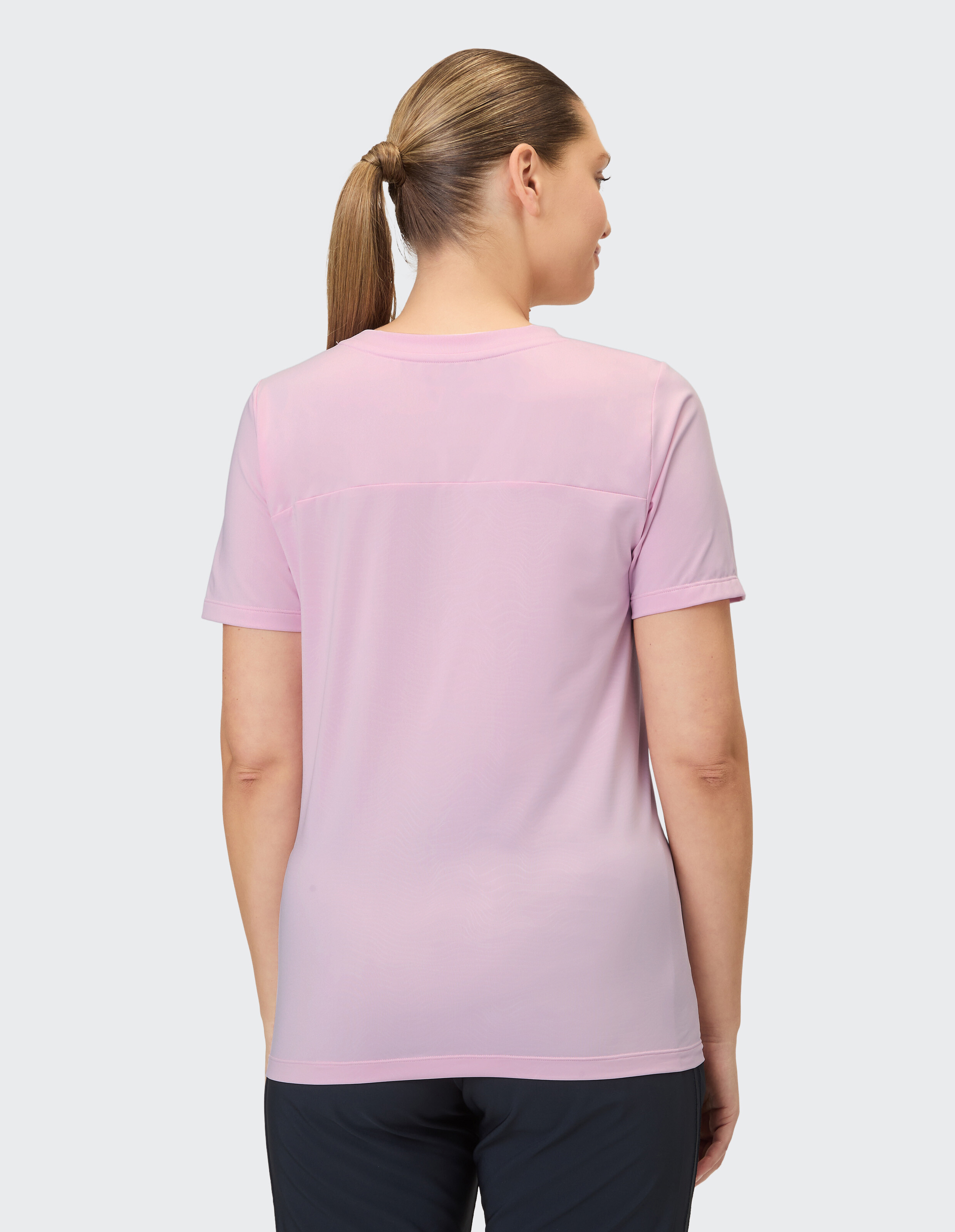 Eine Frau mit einem Pferdeschwanz trägt ein fliederfarbenes T-Shirt mit kurzen Ärmeln und einer dezenten horizontalen Naht im Schulterbereich.