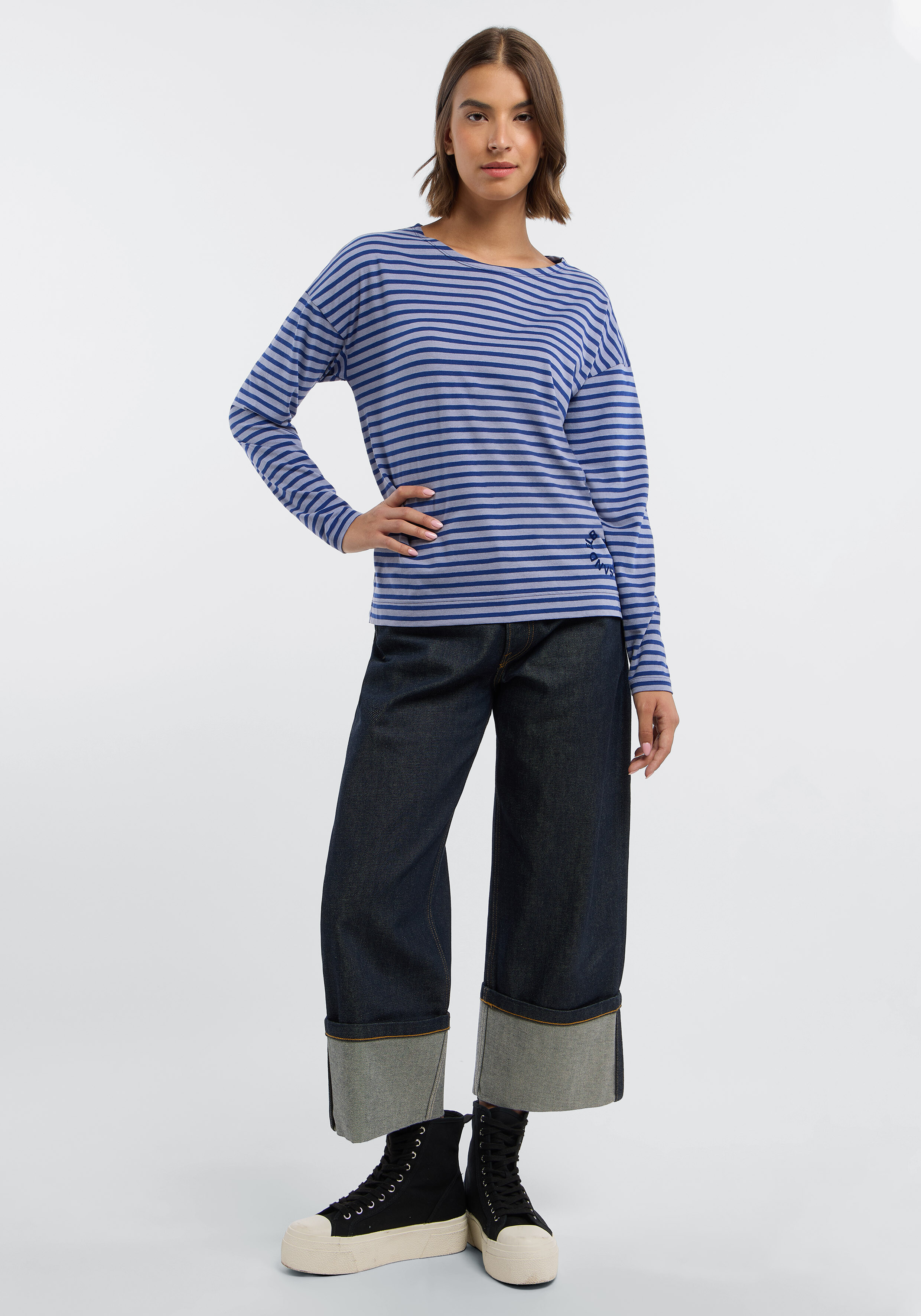 Frau trägt ein gemütliches, blau gestreiftes Langarmhemd und Jeans mit weitem Bein für einen lässigen Stil.