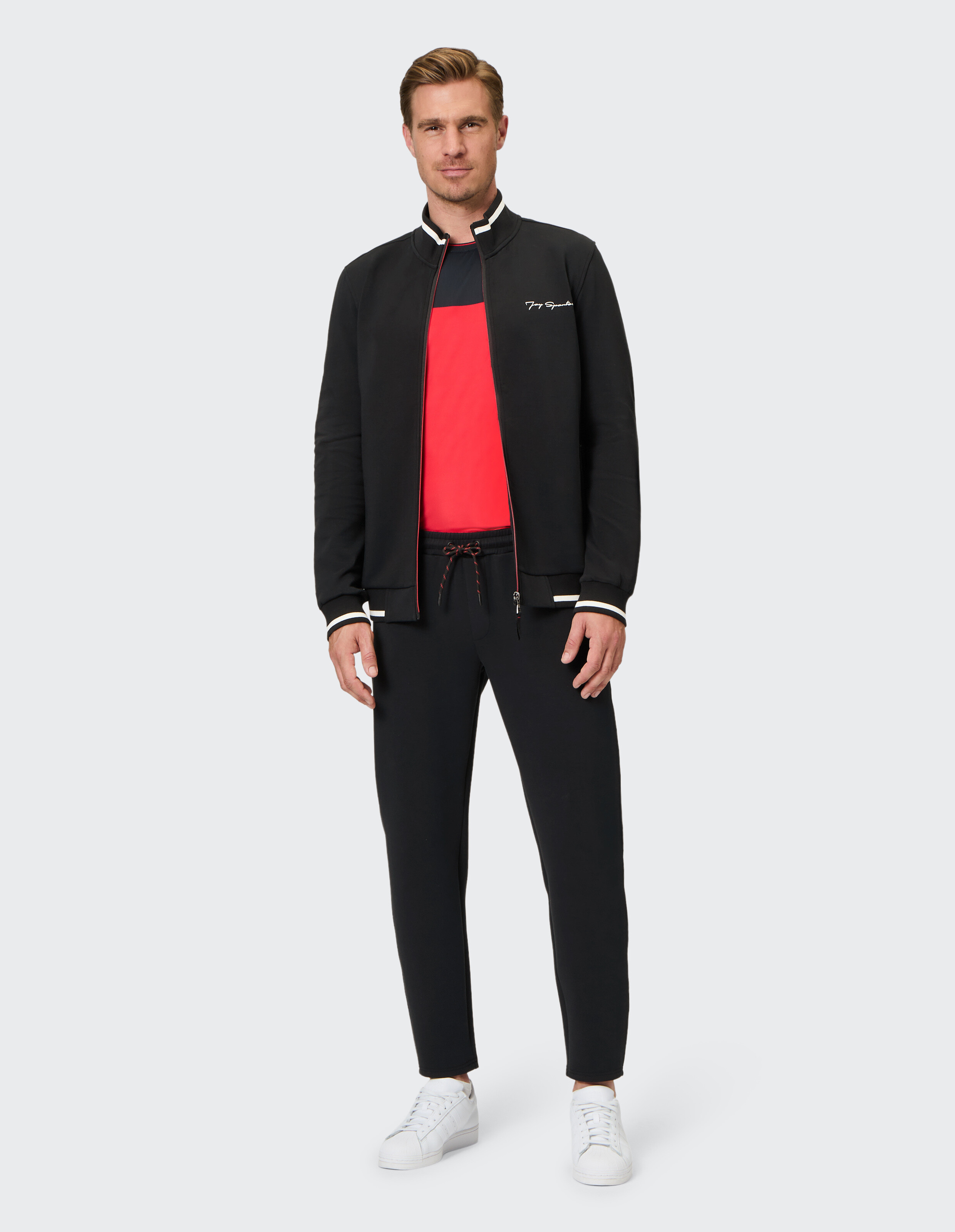 Mann trägt eine schwarze ELBSAND-Trainingsjacke mit Reißverschluss und eine passende schwarze Freizeit-Jogginghose.