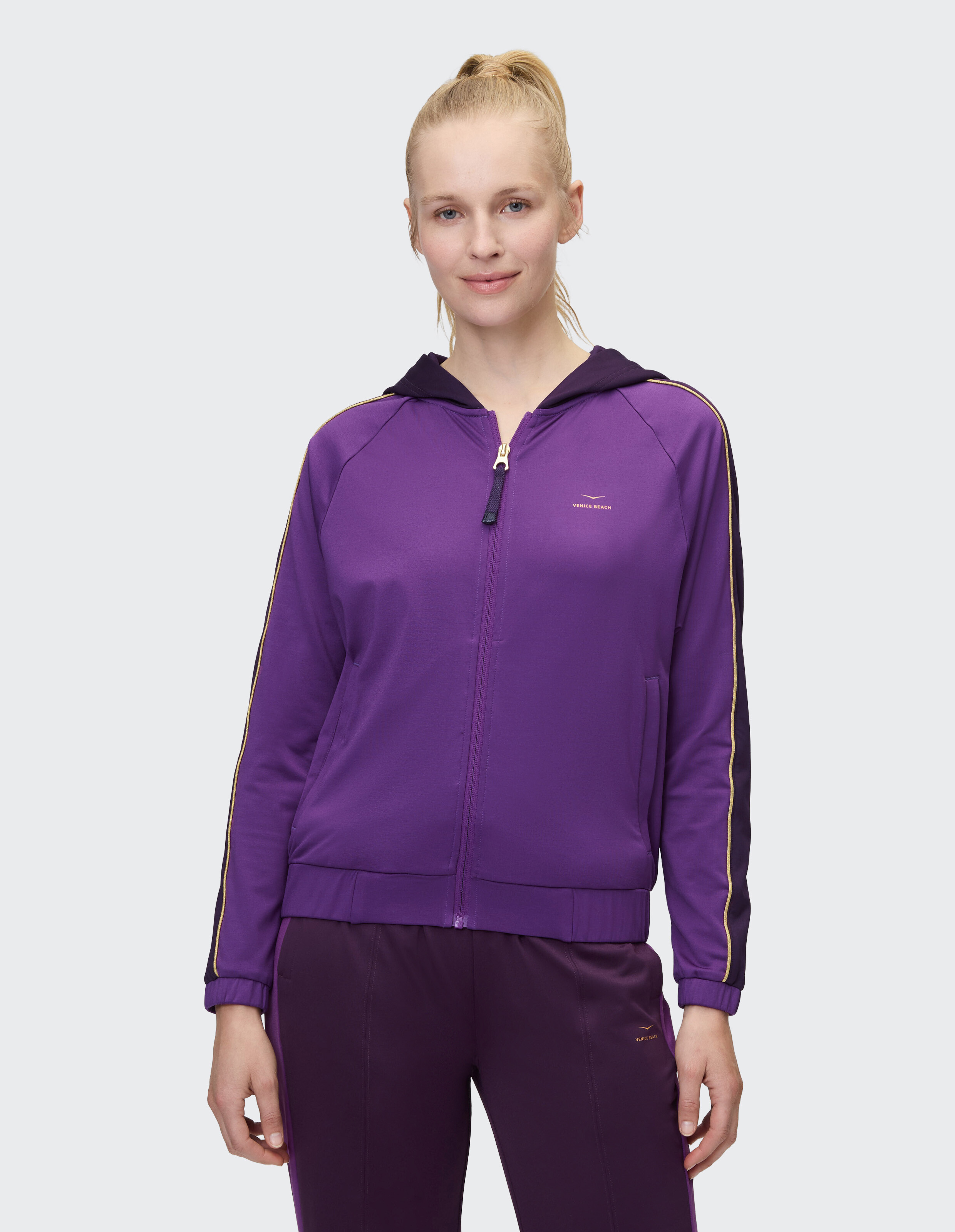 Frau trägt einen lilafarbenen, funktionellen Kapuzenpullover von Venice Beach Gwendolyn mit Reißverschluss für Freizeitkleidung.
