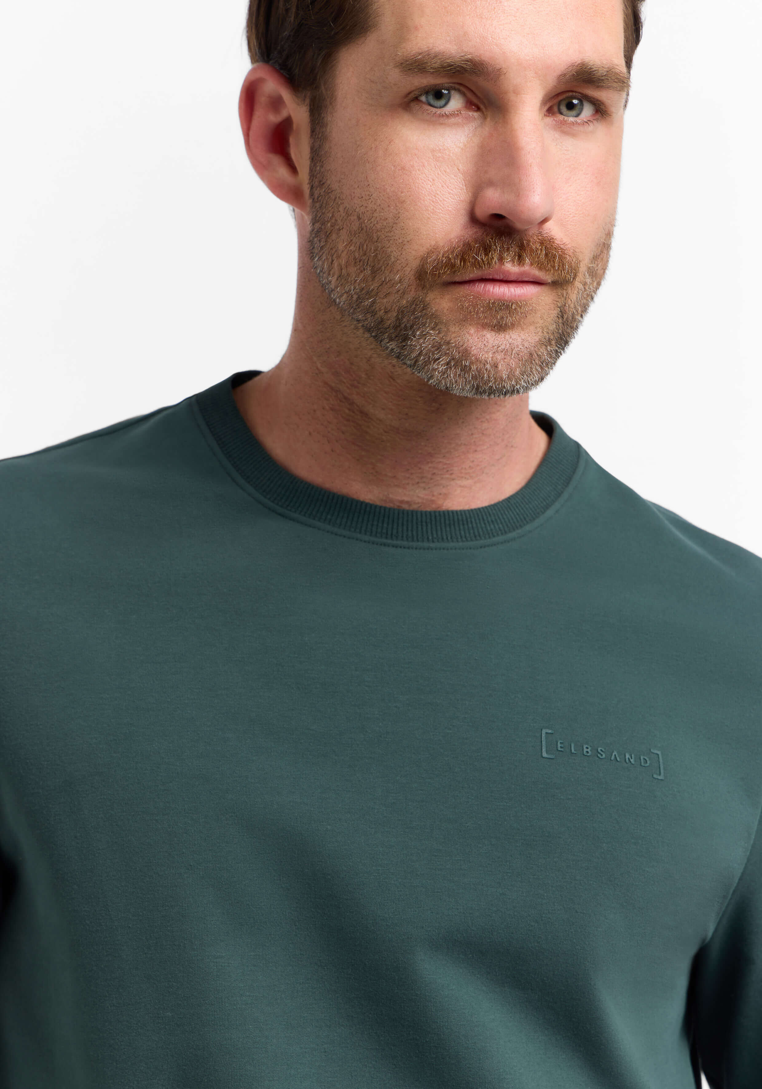 Mann trägt ein dunkelgrünes ELBSAND-Sweatshirt mit Rundhalsausschnitt für lässigen Komfort.