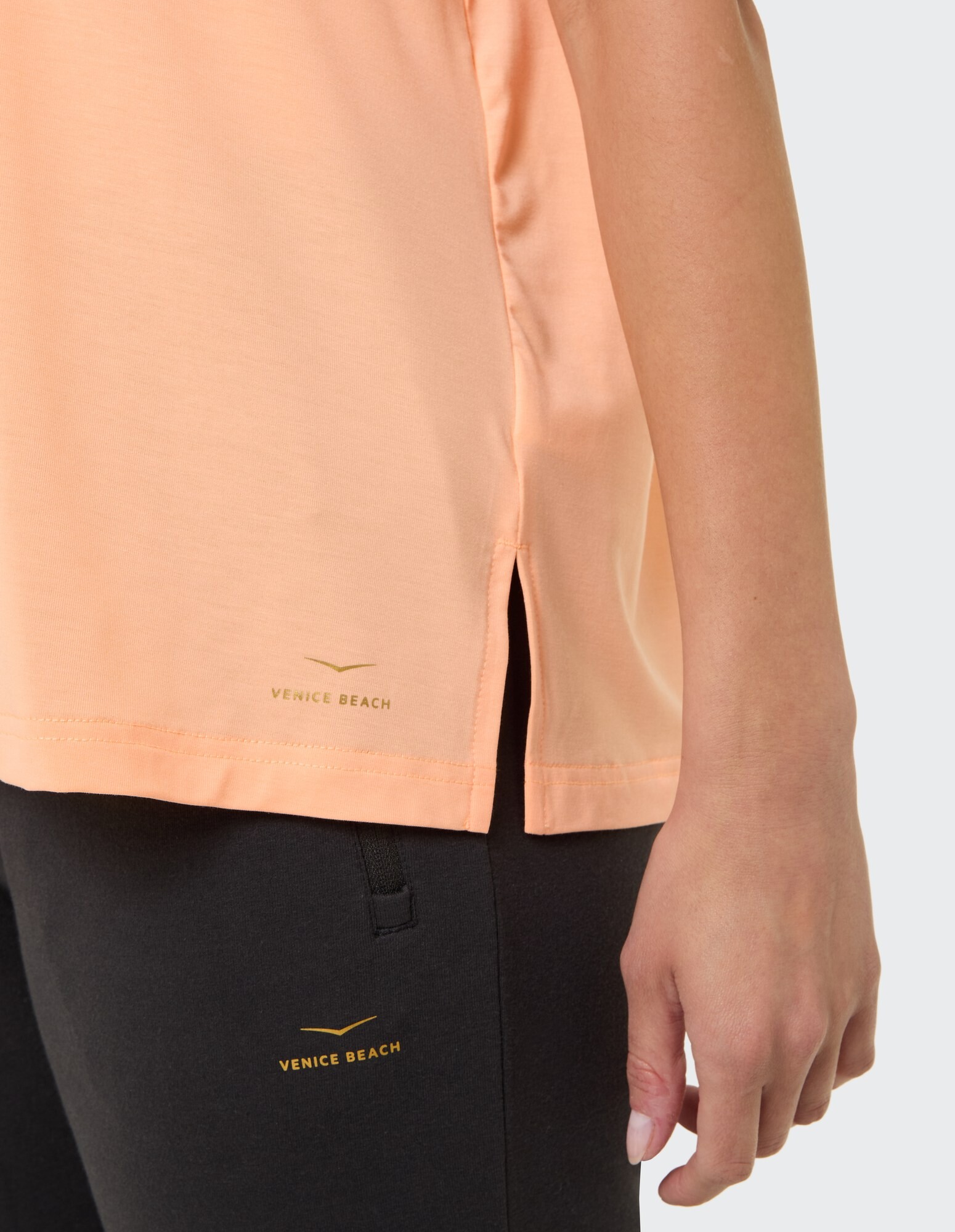 Nahaufnahme eines pfirsichfarbenen Oberteils mit Seitenschlitzen, gepaart mit einer schwarzen Hose.