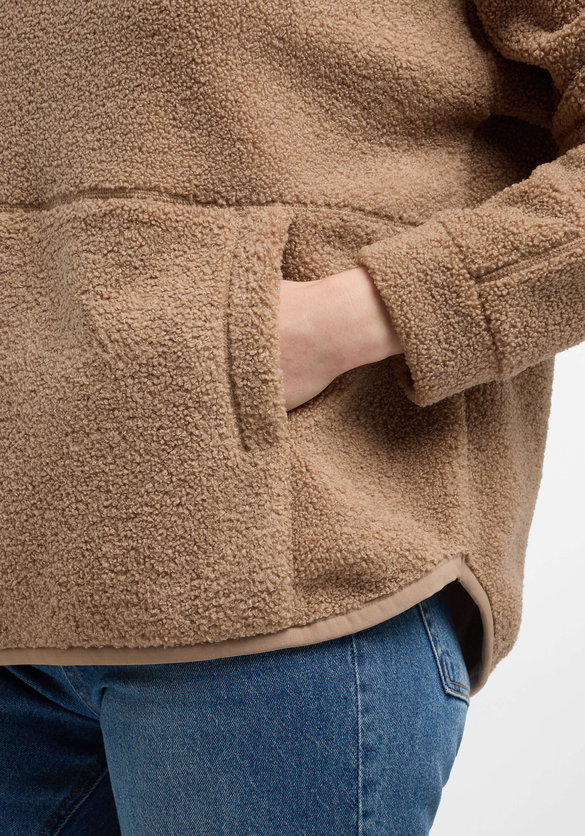 Nahaufnahme eines kuscheligen beigen Teddyfleece-Pullovers mit Tasche, getragen zu Blue Jeans.