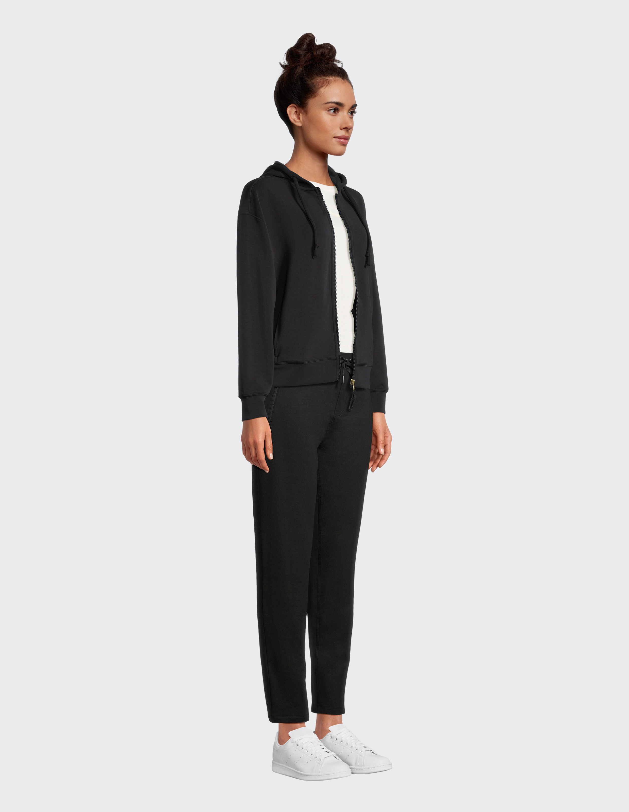 Frau in einem schwarzen Kapuzenpullover mit Reißverschluss und passenden Jogginghosen für gemütliche, elegante Freizeitkleidung.