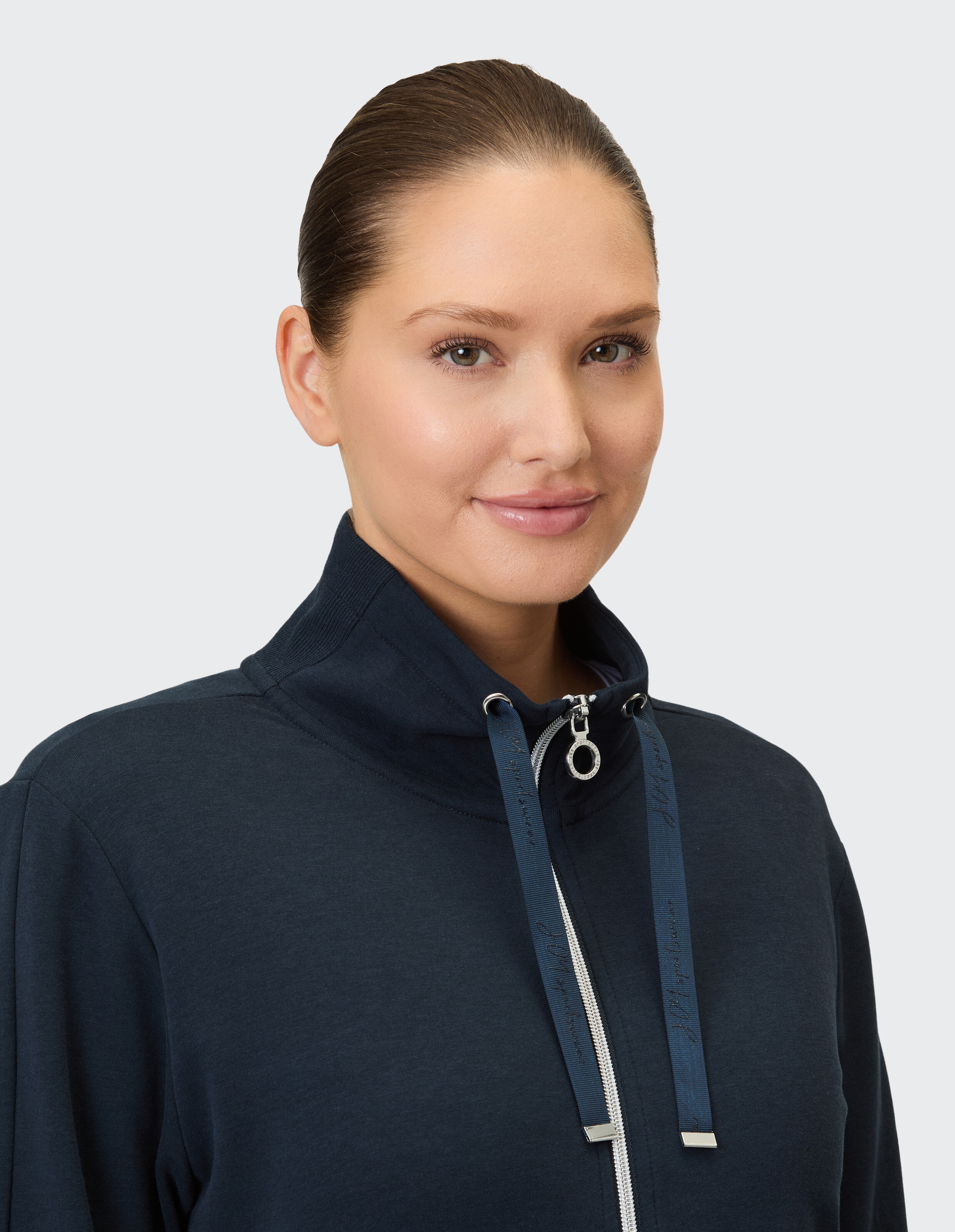 Nahaufnahme einer Frau in einem marineblauen Kapuzenpullover mit Reißverschluss und modischen Kordelzügen.
