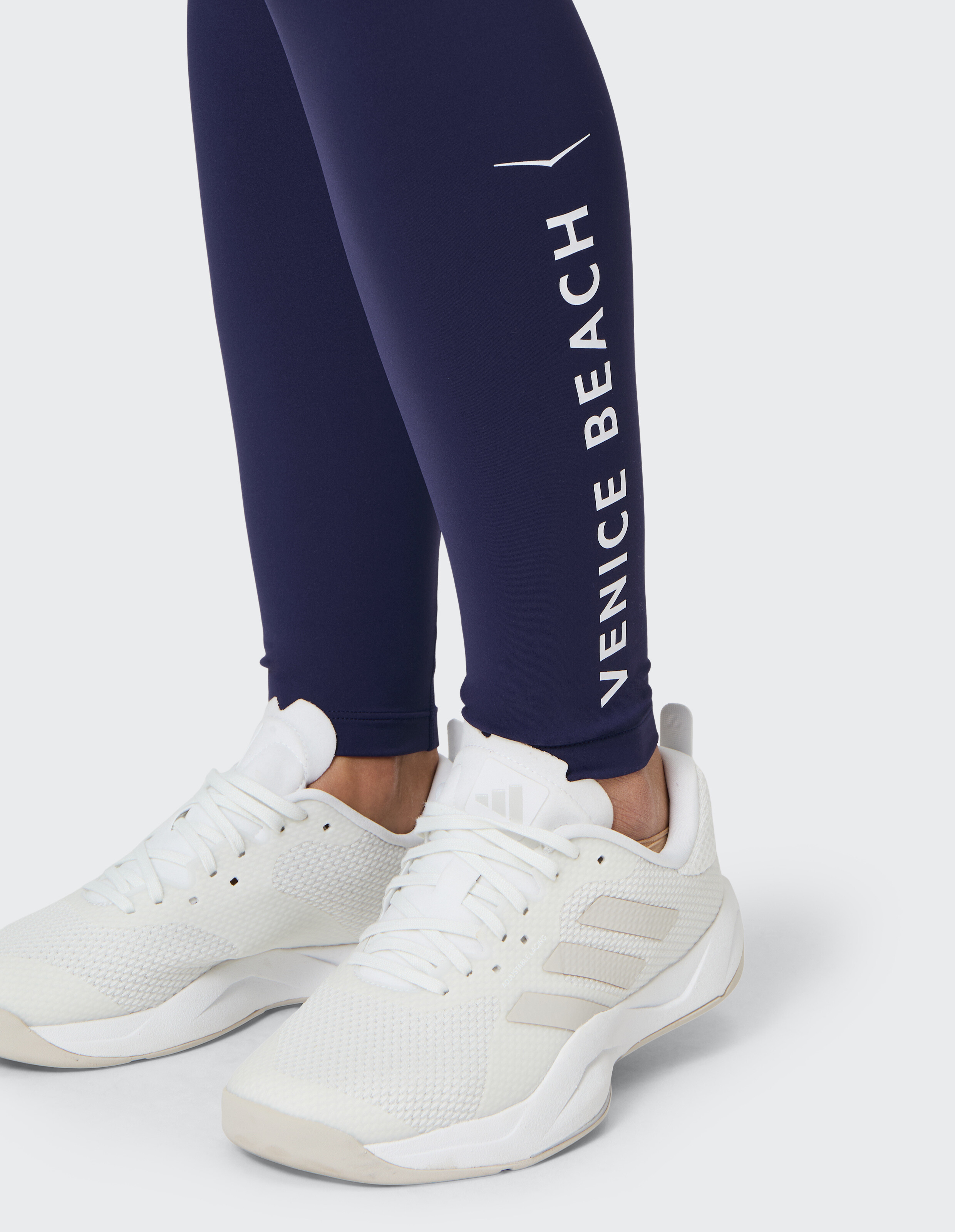 Marineblaue Leggings mit weißem Venice Beach-Logo, getragen mit weißen Freizeit-Sneakern.