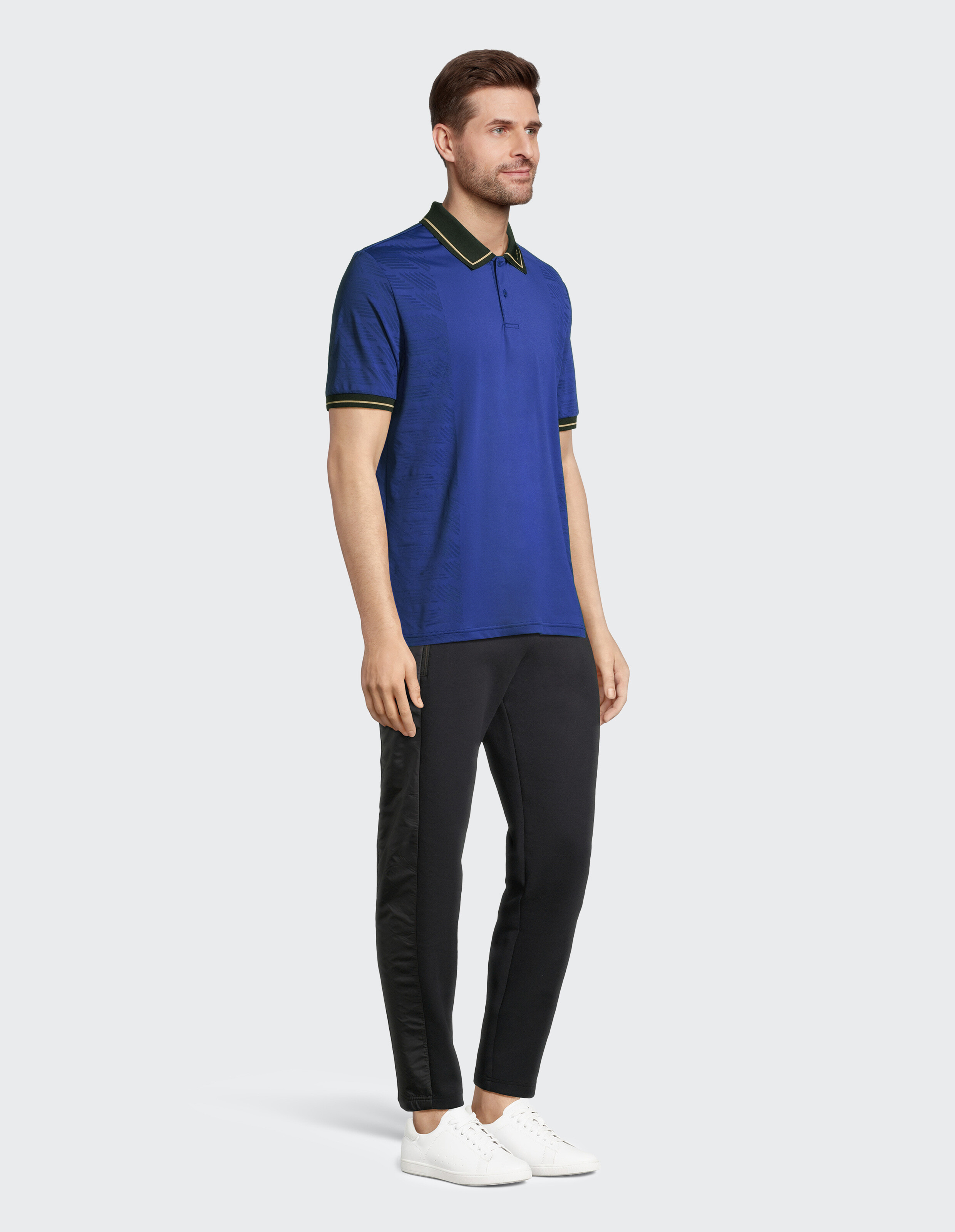 Mann in einem blauen Poloshirt mit grünem Besatz und schwarzen Jogginghosen, lässig gestylt.