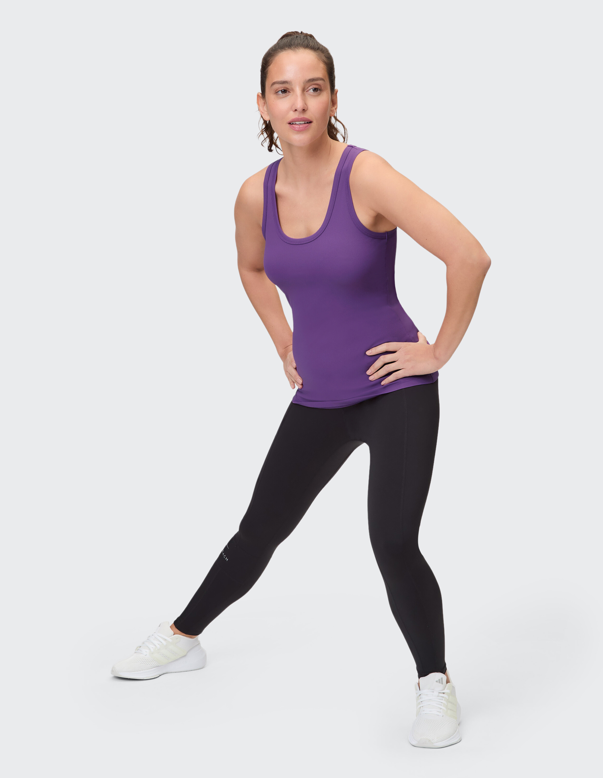Frau in einem lila Tanktop und schwarzen Leggings posiert für lässige Fitnesskleidung.