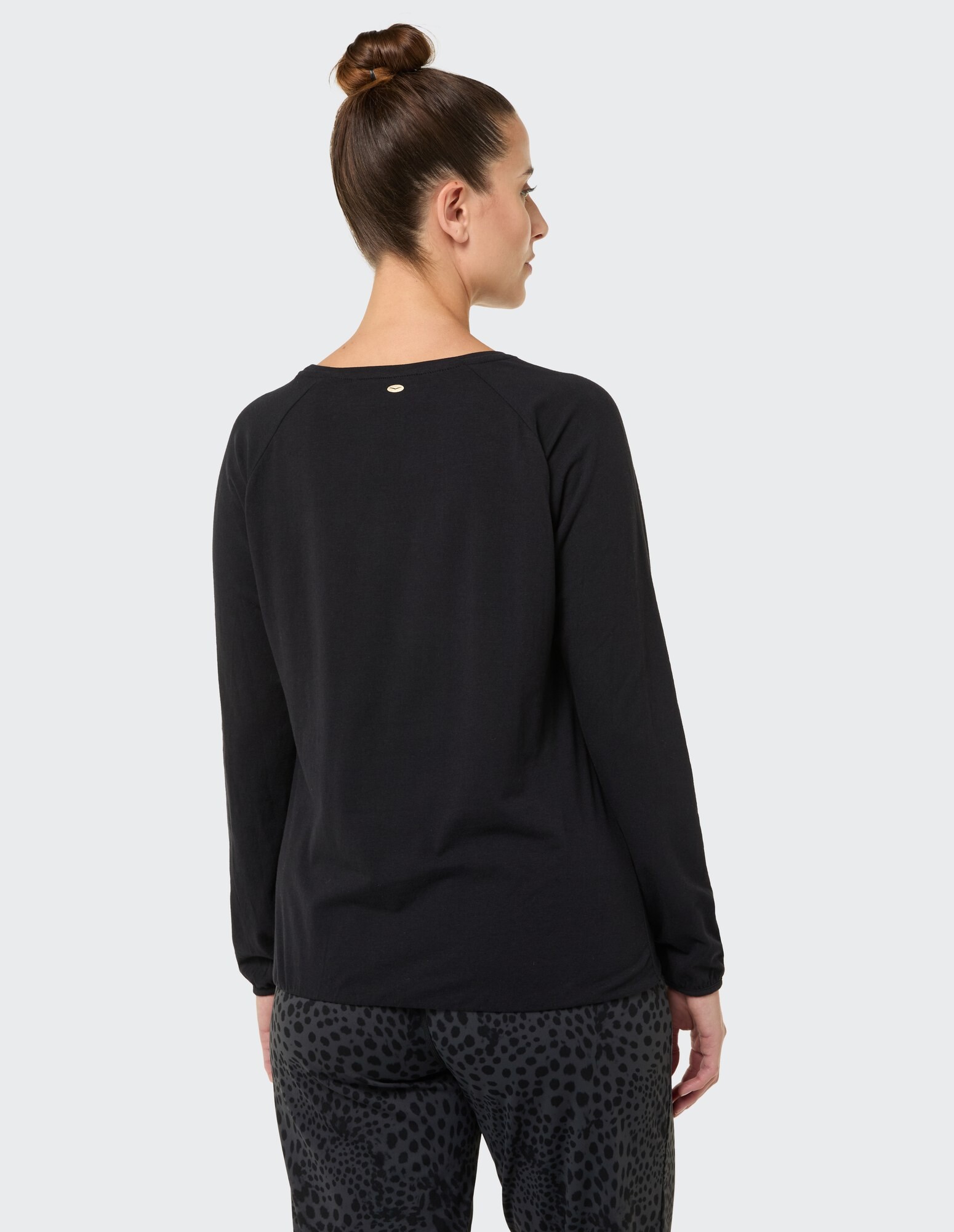 Rückansicht einer Frau in einem schwarzen Langarmshirt und einer gemusterten Hose.