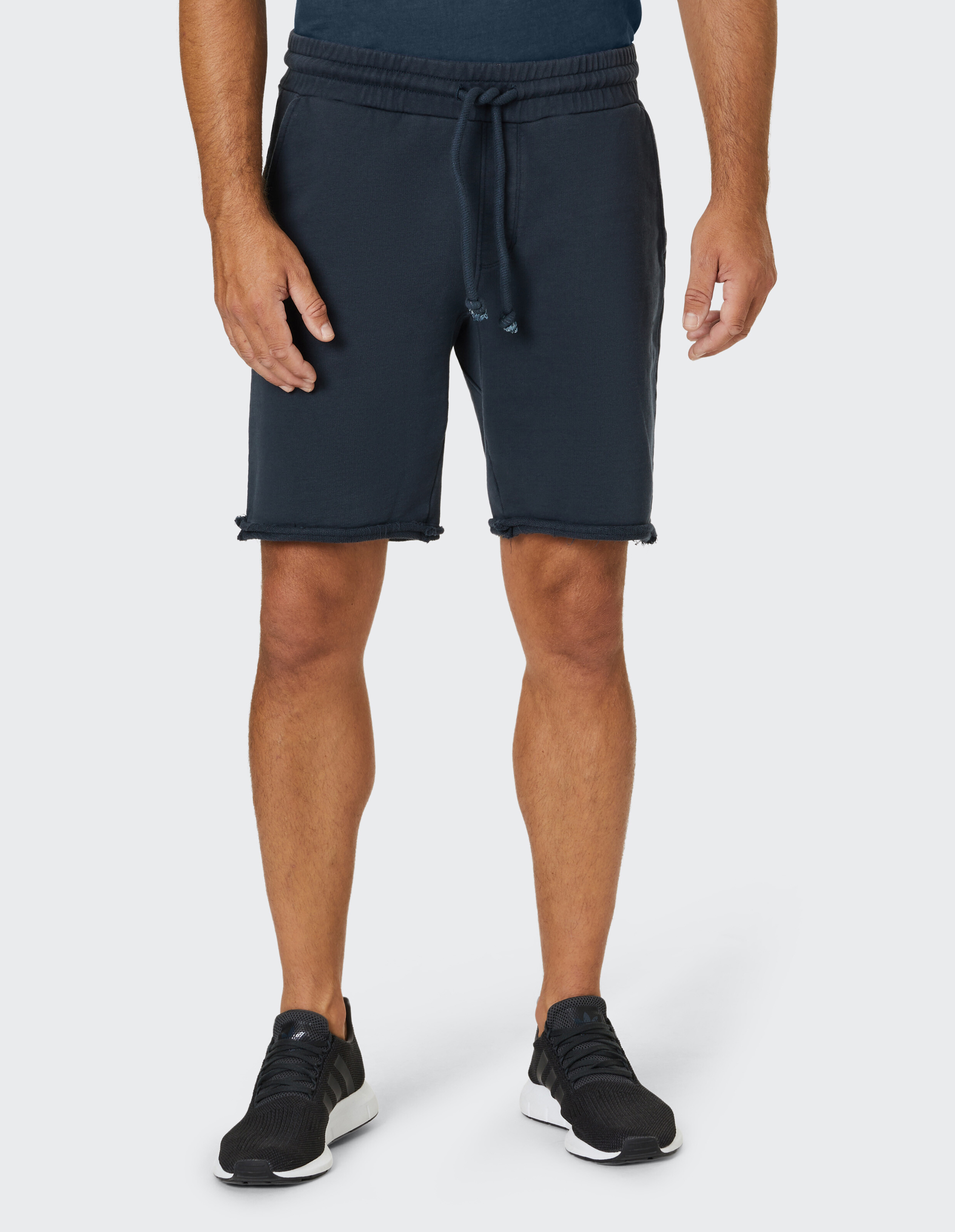 Mann trägt dunkelblaue, lässige Sweatshorts mit Kordelzug in der Taille und ungesäumtem Saum.