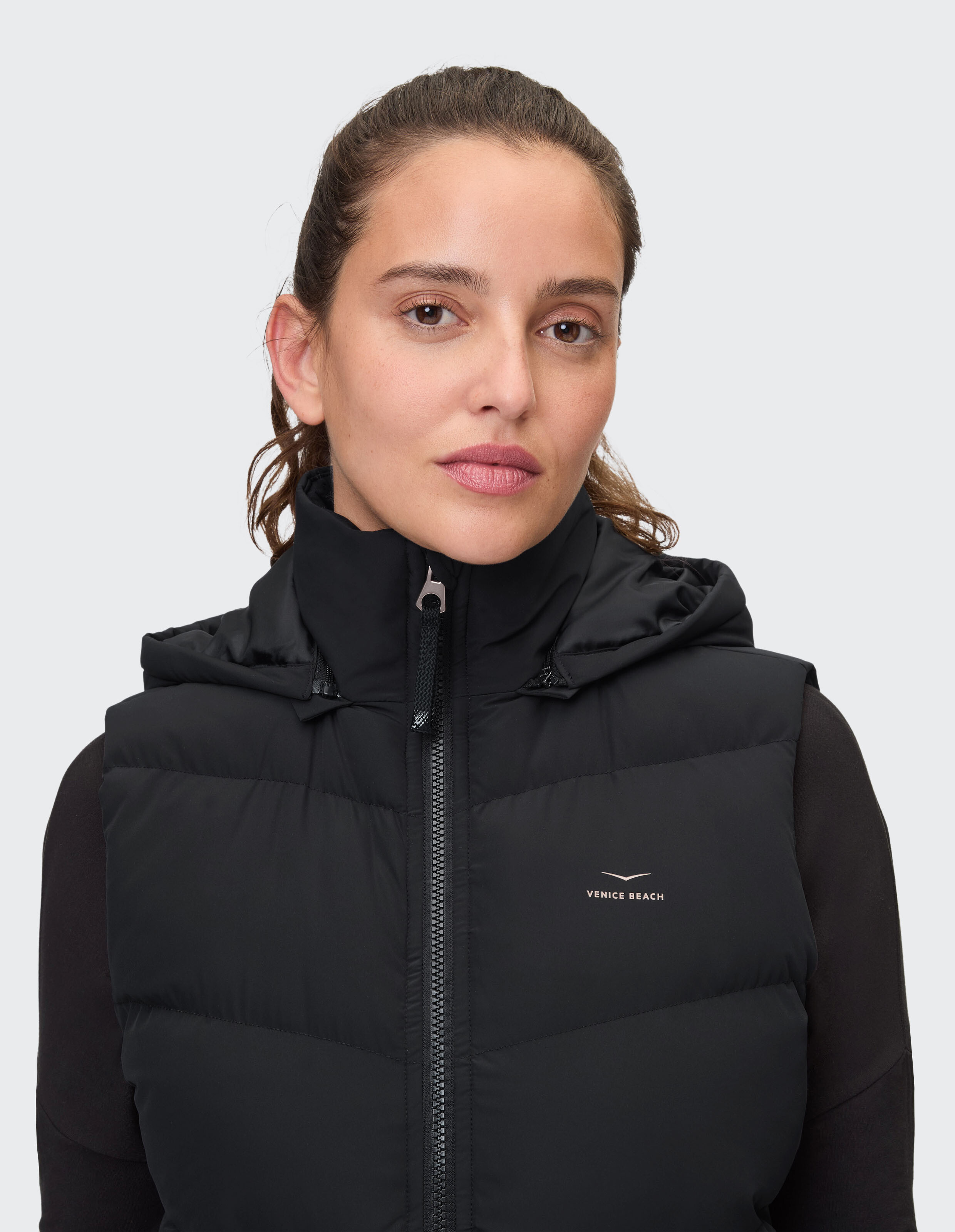 Frau trägt eine schwarze Daunenweste mit Kapuze von Venice Beach für einen lässigen Outdoor-Stil.