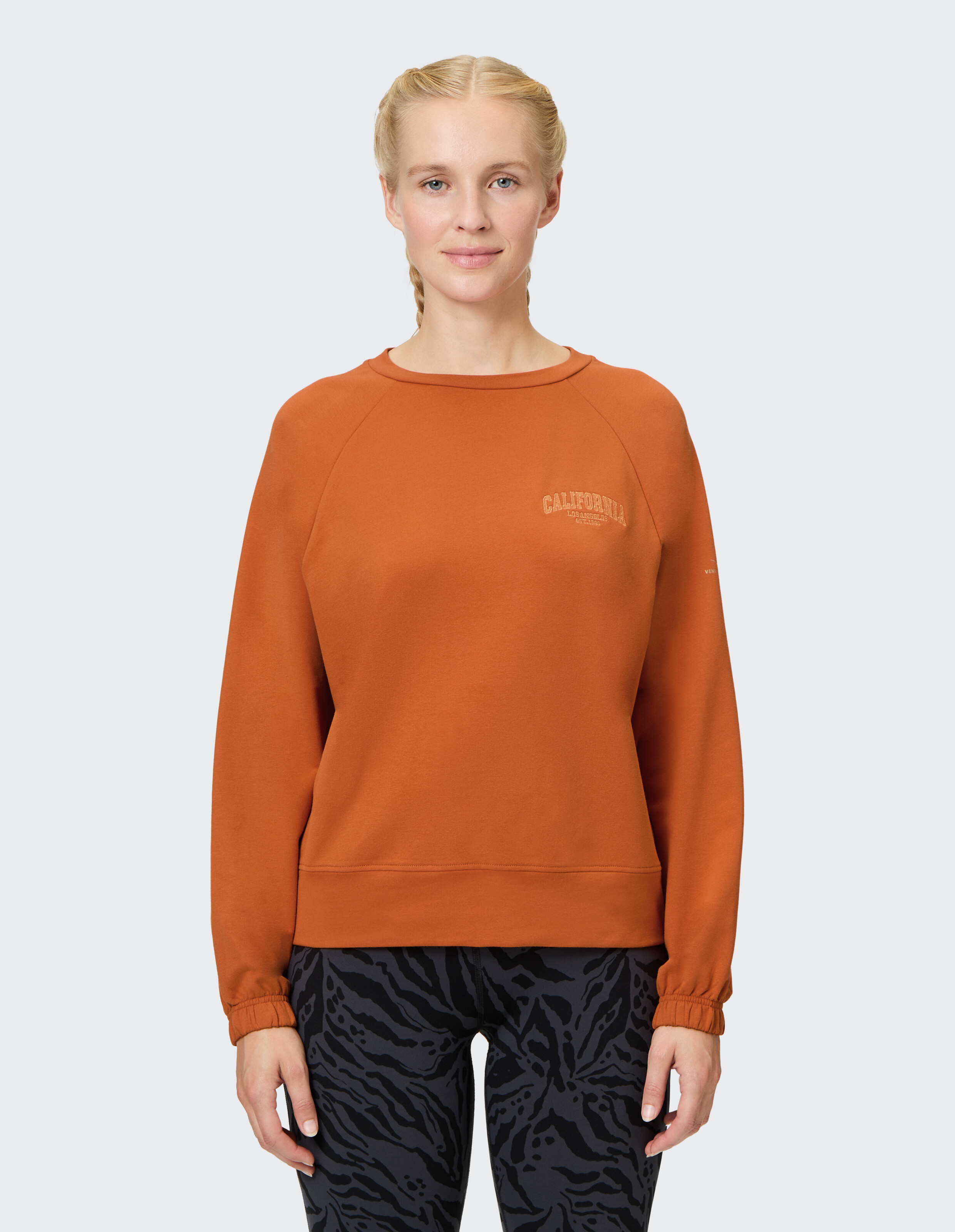 Gemütliches orangefarbenes Sweatshirt mit California-Print, gepaart mit gemusterten Leggings.