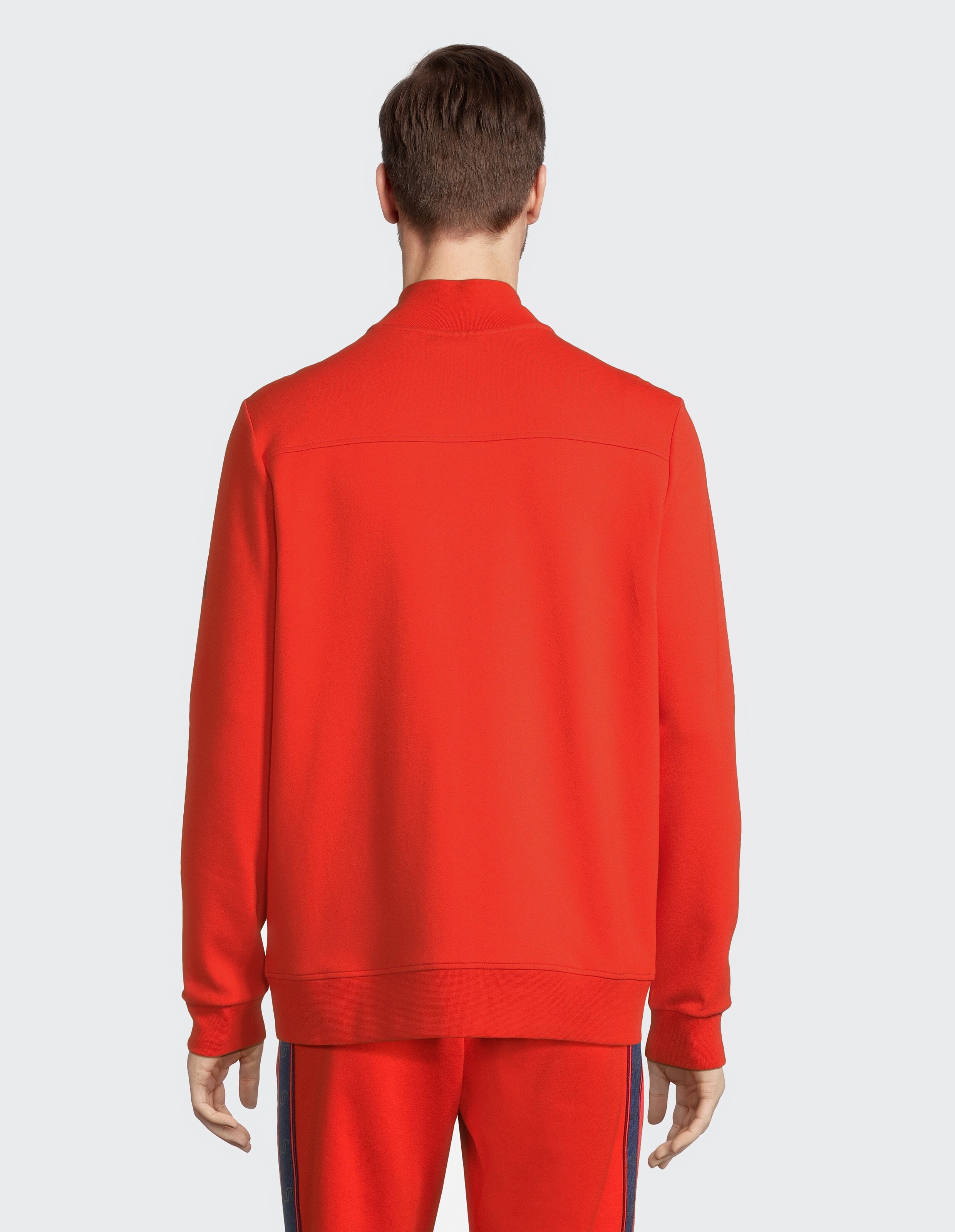 Rückansicht eines Mannes, der zum Faulenzen eine gemütliche rote Freizeitjacke mit Reißverschluss trägt.