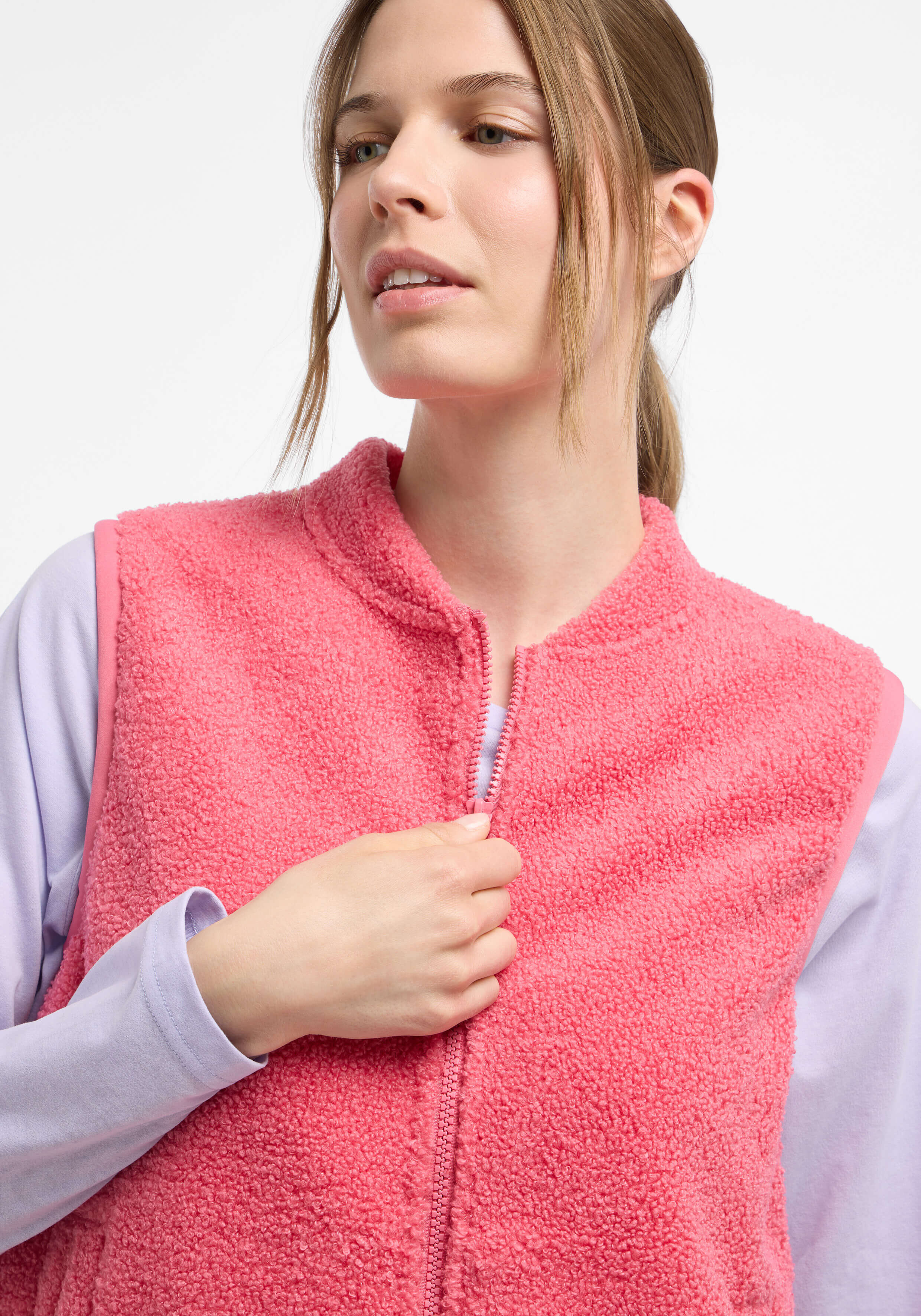 Das Model trägt eine kuschelige rosa Fleeceweste über einem lavendelfarbenen Langarmhemd.