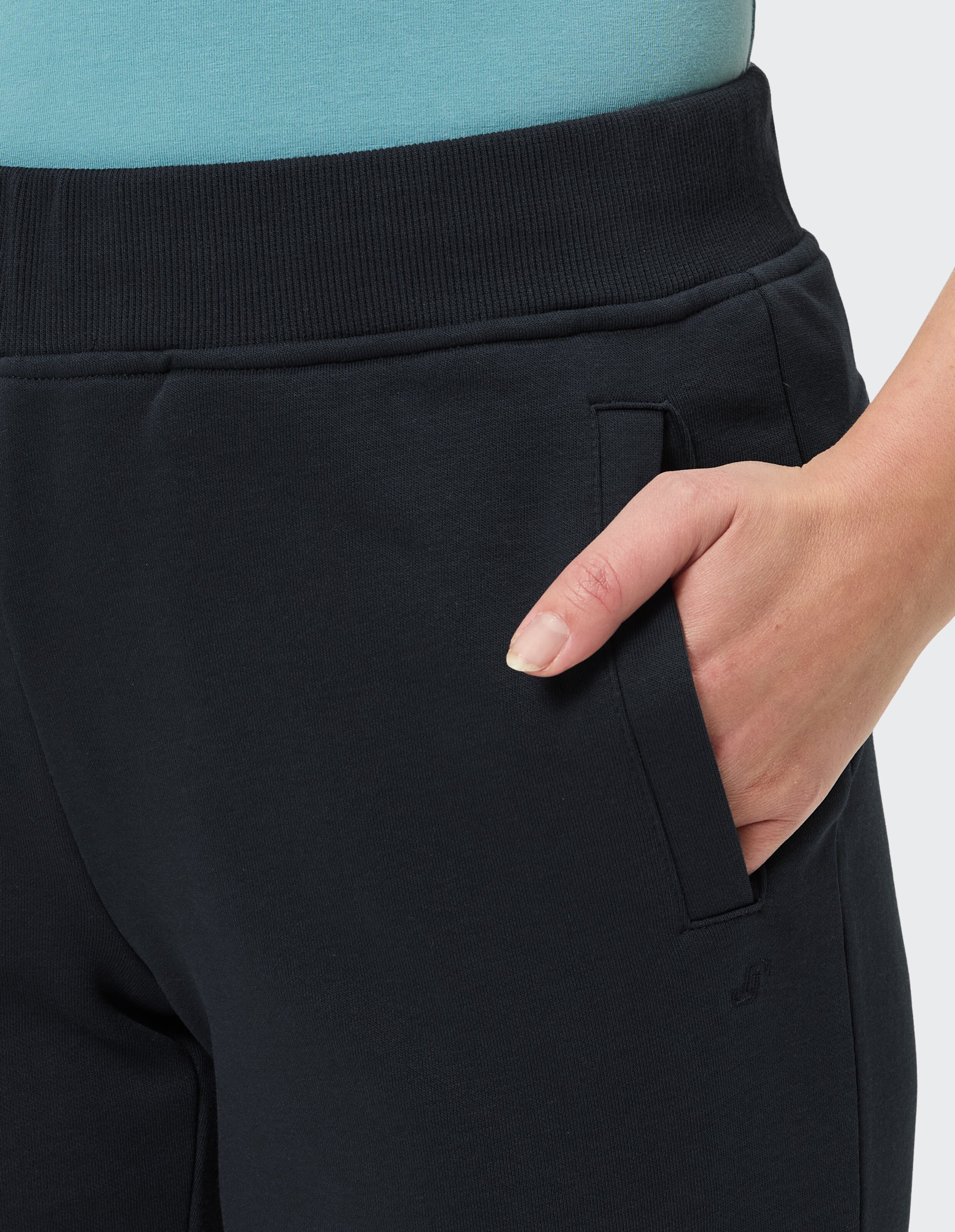 Nahaufnahme einer marineblauen Jogginghose, in deren Tasche eine Hand steckt, mit elastischem Bund und kleinem Logo am Bein.