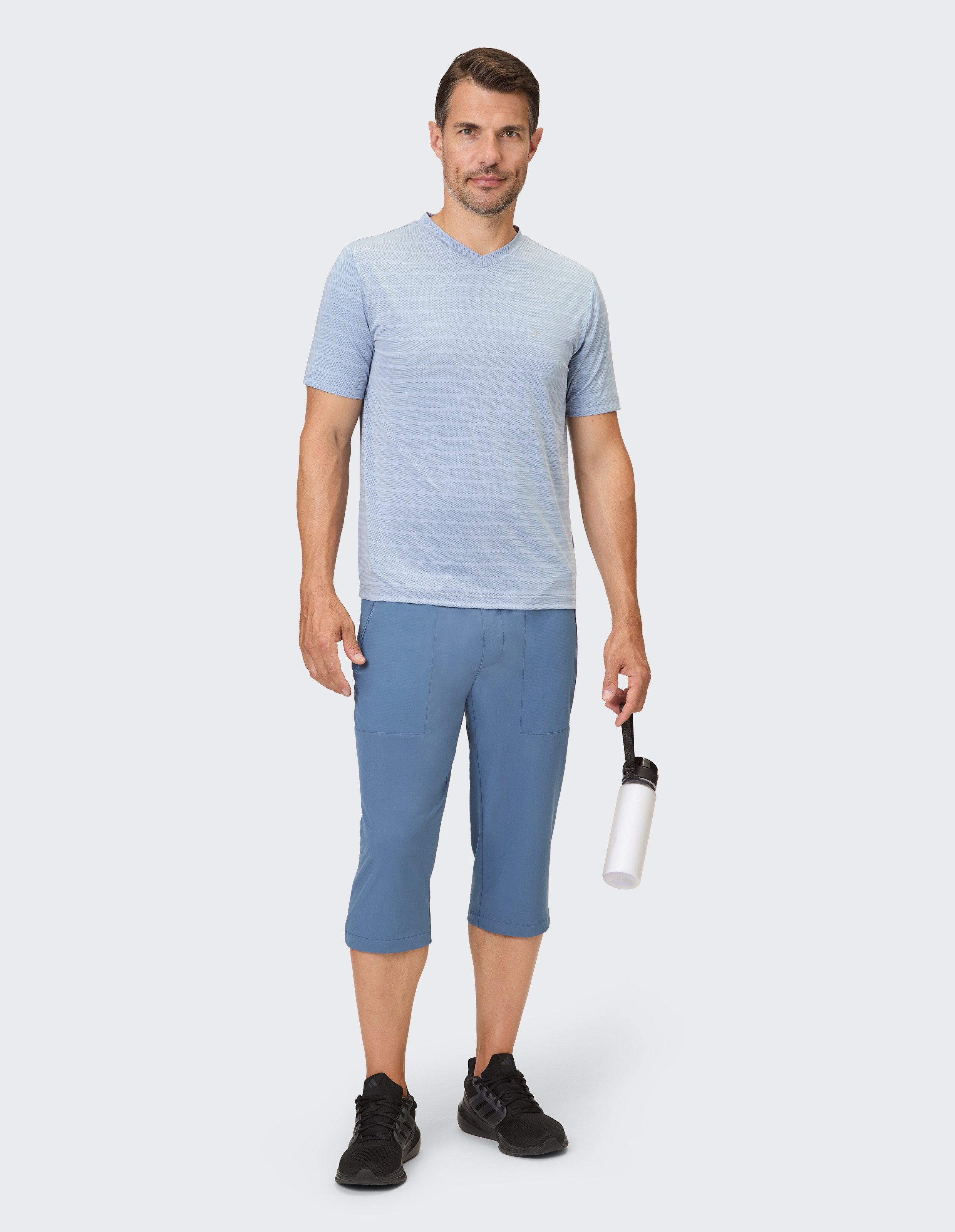 Ein Mann mit kurzen, blau gestreiften Ärmeln und blauen Dreiviertelhosen trägt einen weißen Trinkflasche.
