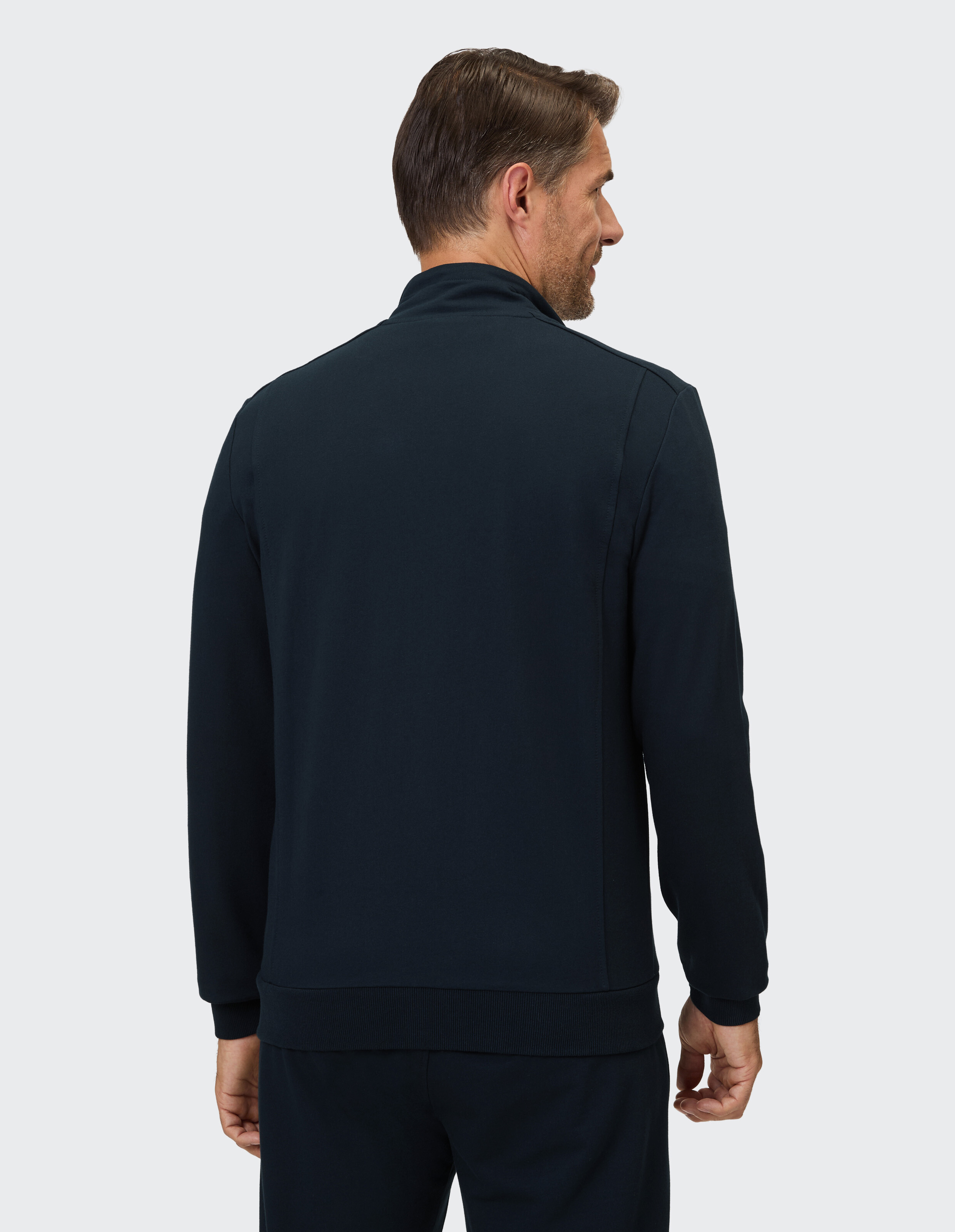 Der Mann trägt eine dunkelblaue Jacke mit Stehkragen und einem Gummibund am Saum.