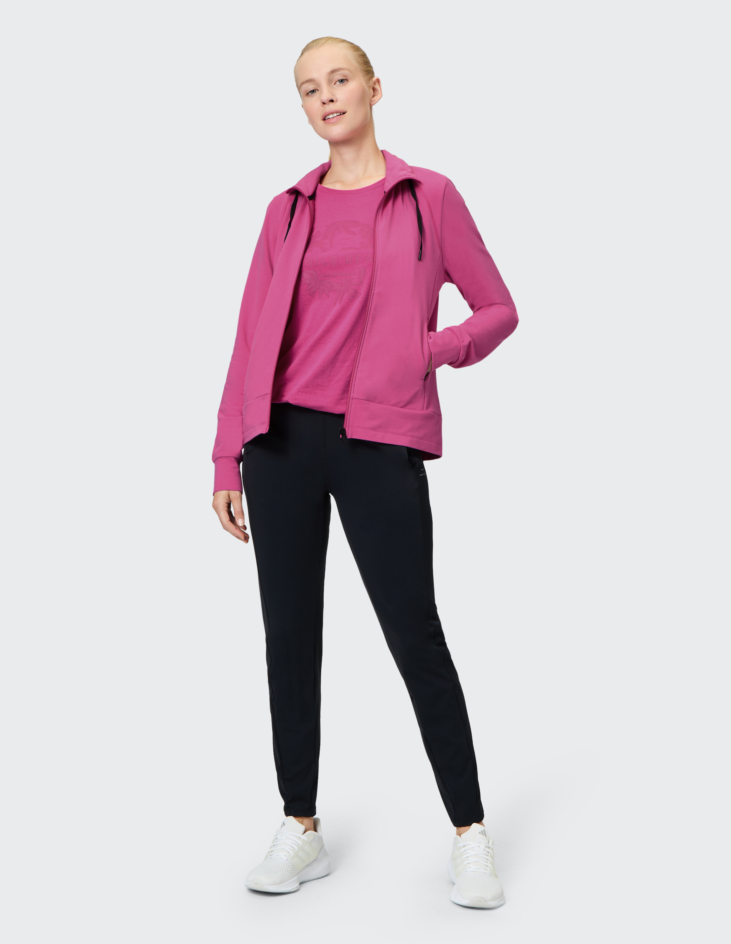 Frau in einem rosa Kapuzenpullover mit Reißverschluss und einer schwarzen Hose, lässig gestylt.