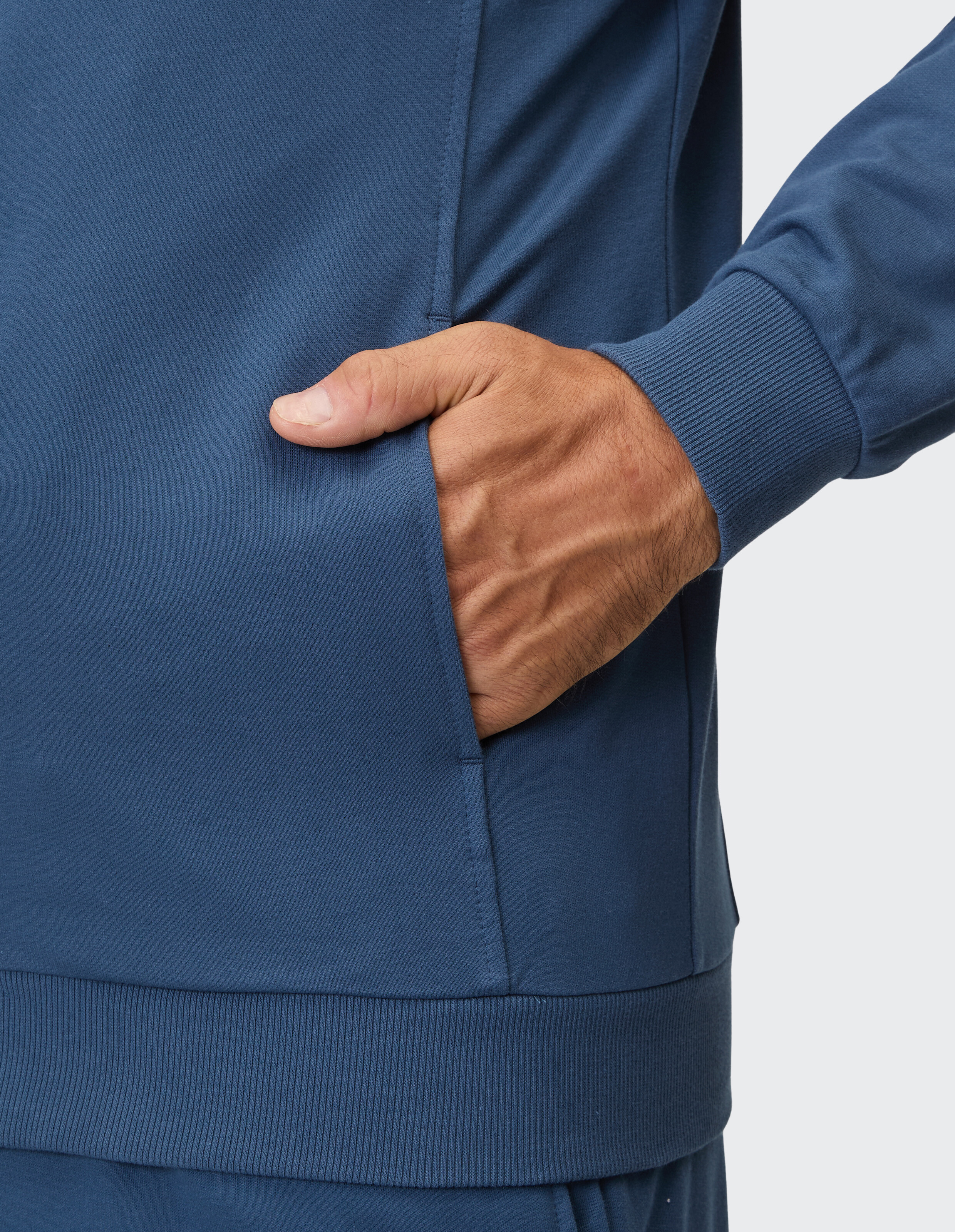 Eine Person steckt die Hand in die Tasche eines blauen Kapuzenpullovers mit Rippbündchen.
