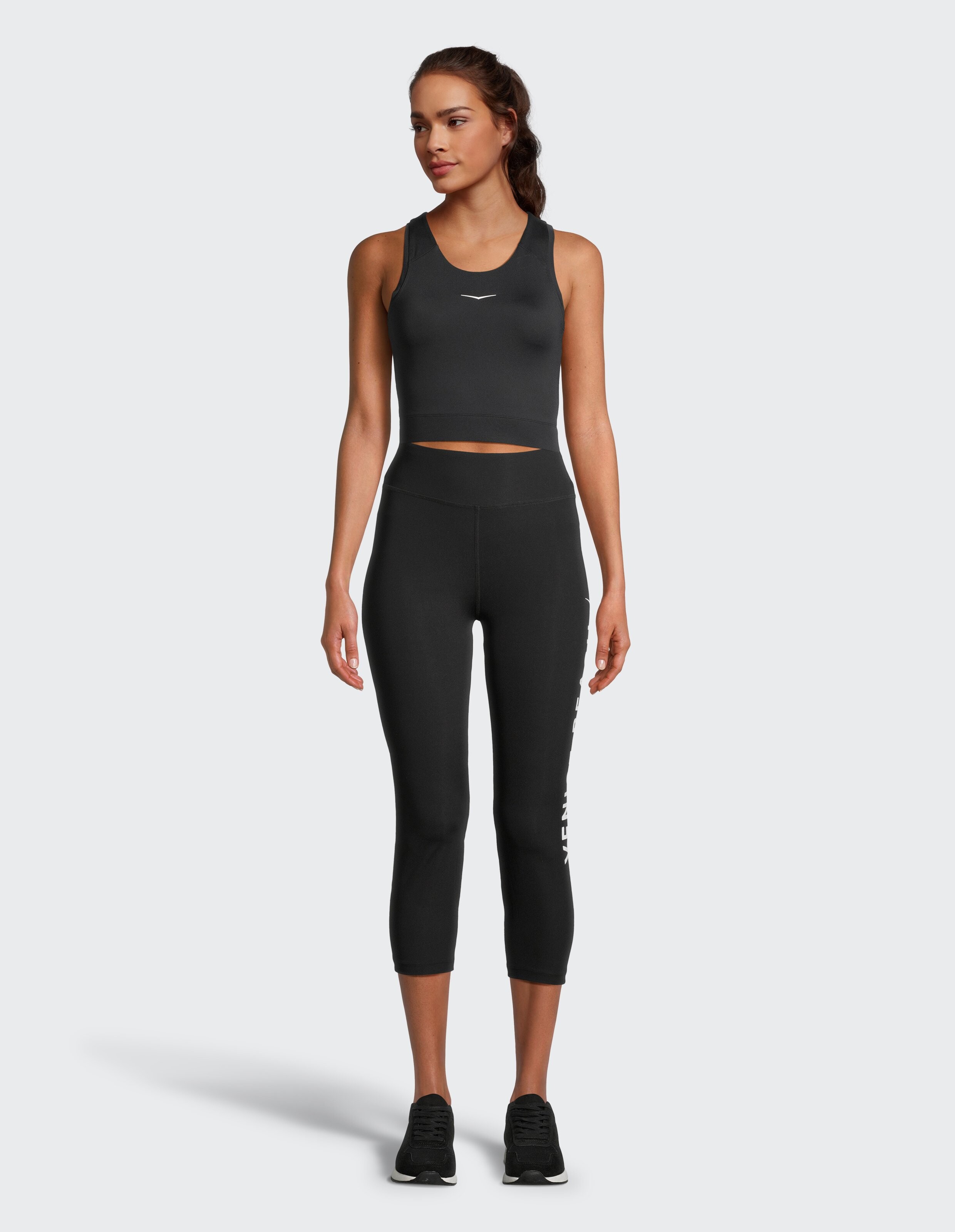 Das Model trägt ein schwarzes, kurzes Tanktop und passende Capri-Leggings.