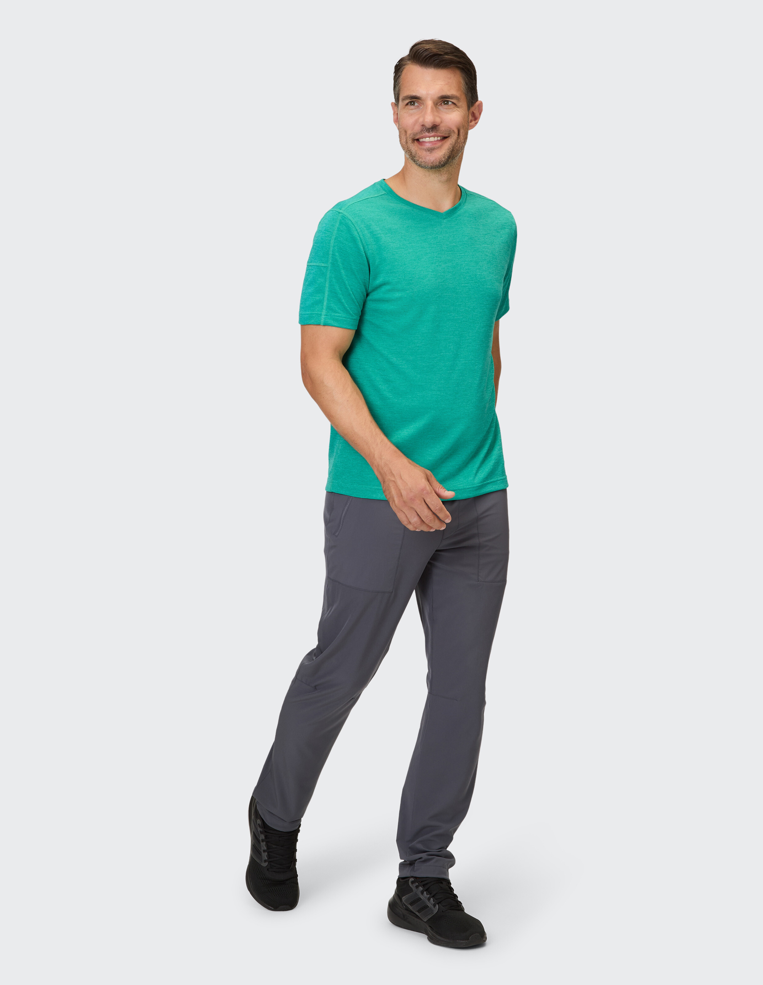 Mann in grünem T-Shirt mit V-Ausschnitt und grauer Hose zeigt lässigen Stil.