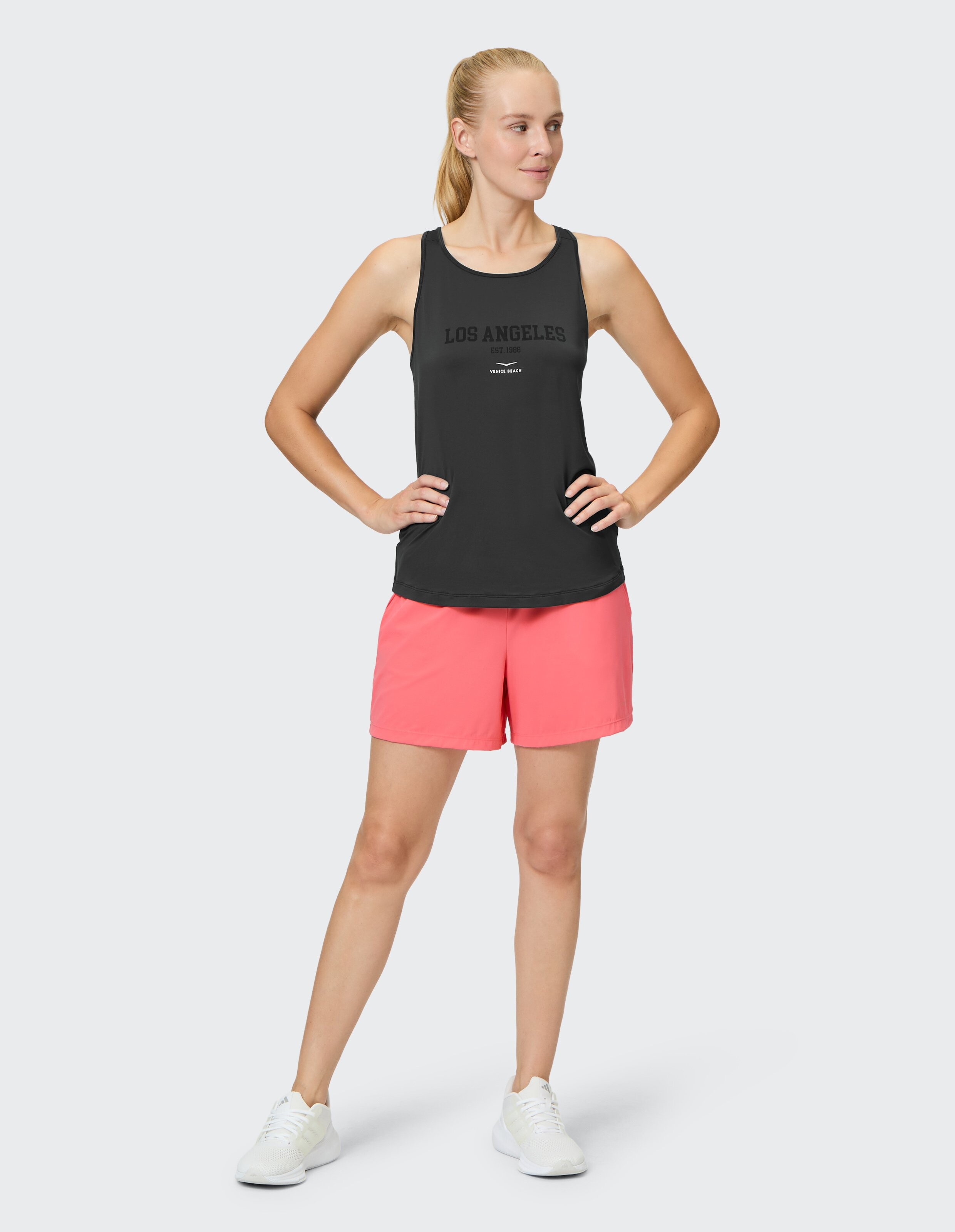 Frau in schwarzem Tanktop und rosa Shorts präsentiert lässigen Sommerstil.
