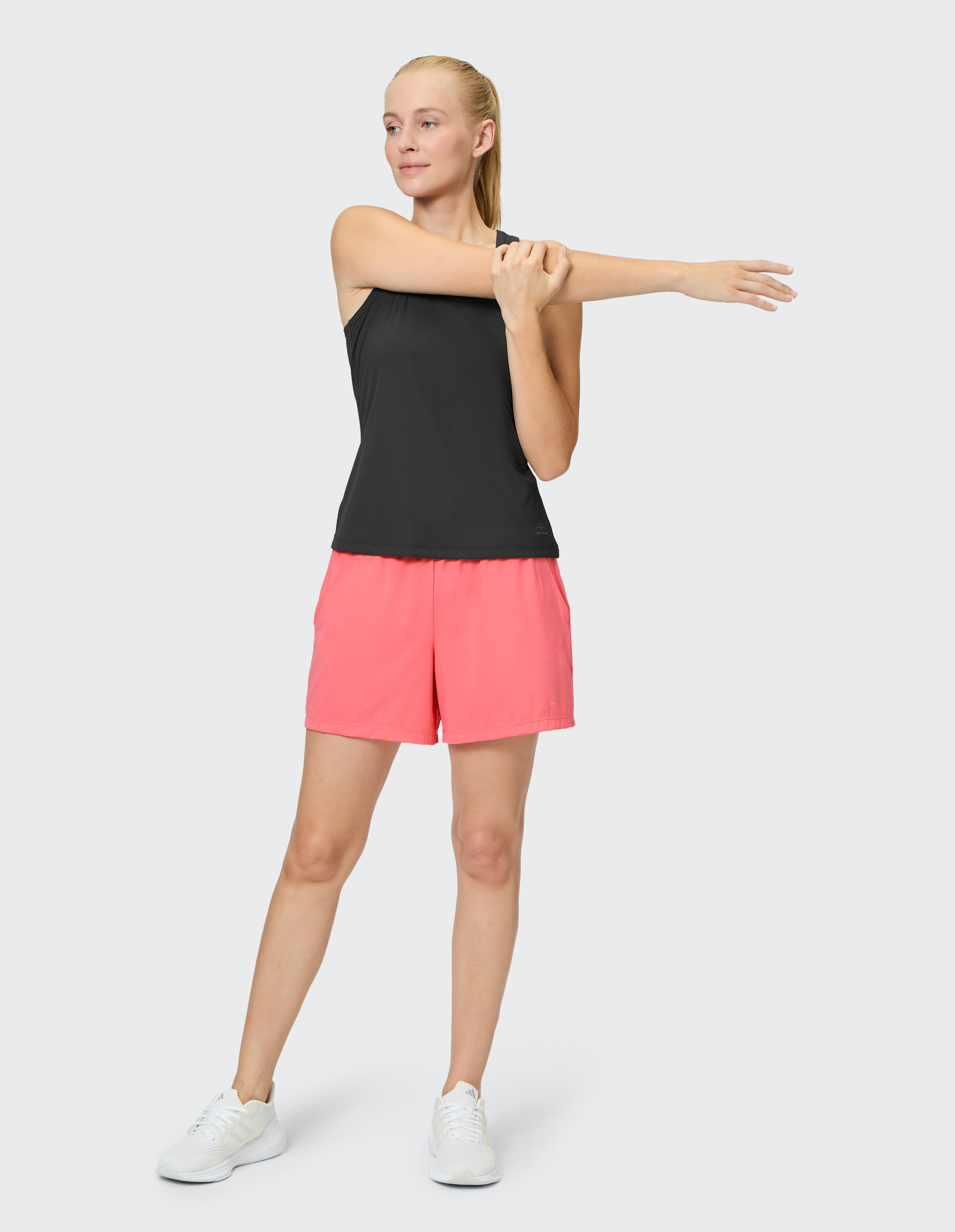 Frau dehnt sich in einem schwarzen Tanktop und rosa Shorts, ideal für Freizeitkleidung.
