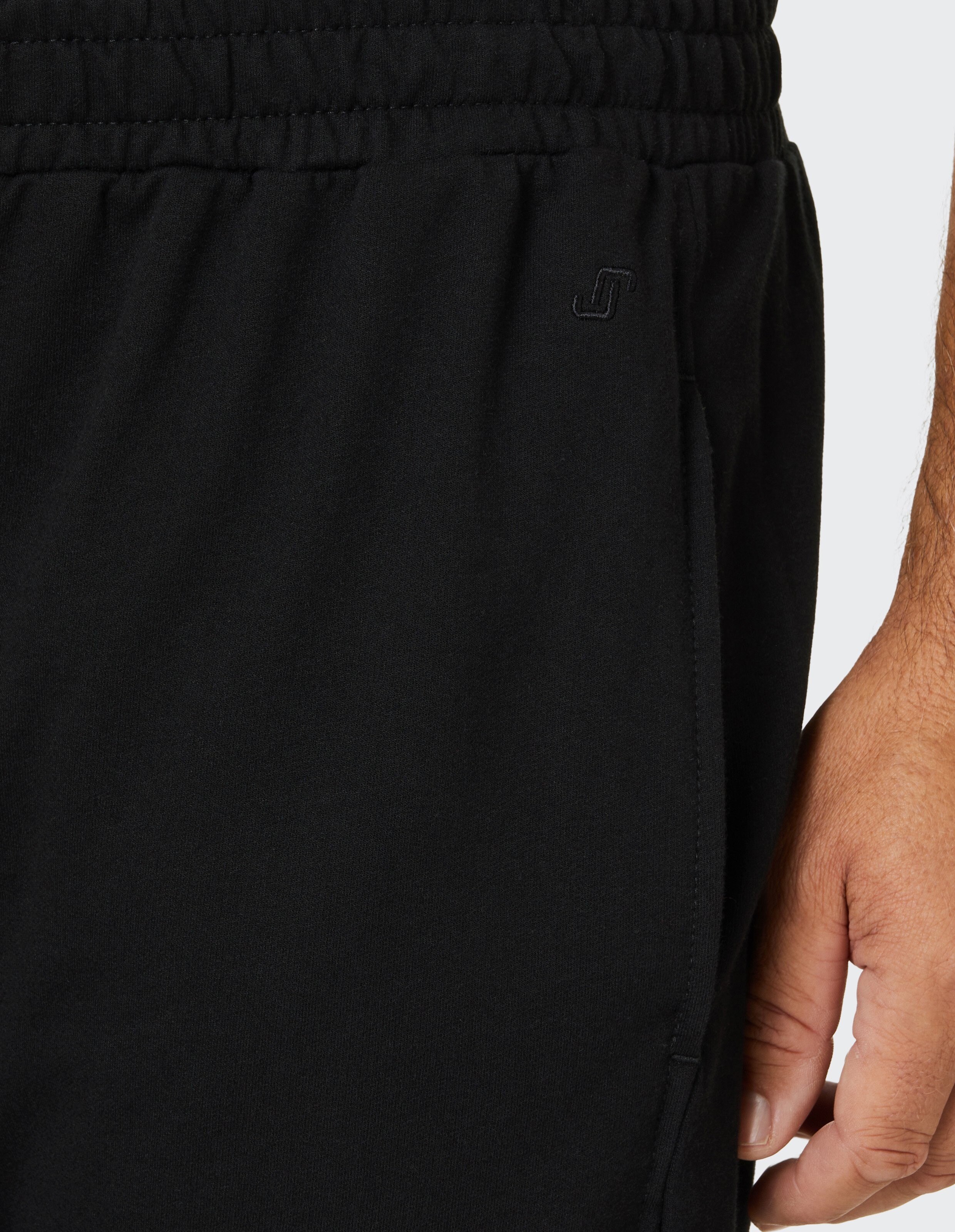 Ein schwarzer Jogginganzug mit elastischem Bund, Tasche und einer Hand daneben, auf weißem Hintergrund.