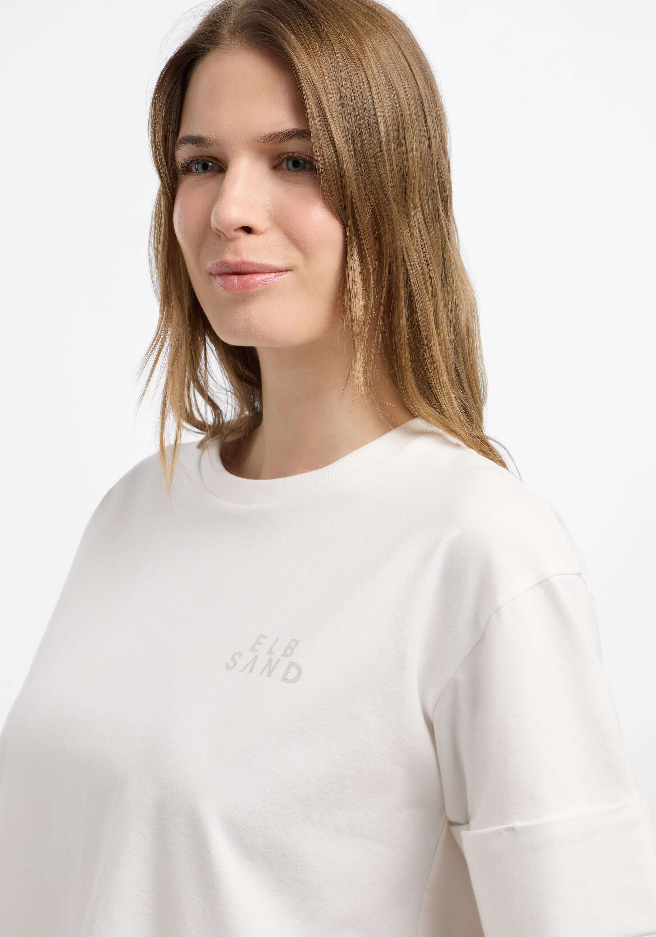 Nahaufnahme einer Frau, die ein hellbeiges ELBSAND-T-Shirt mit entspannter Passform trägt.
