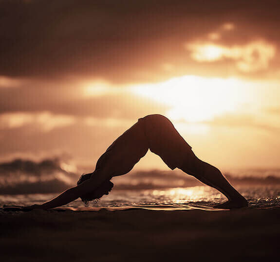 Silhouette einer Person, die bei Sonnenuntergang am Strand Yoga macht.