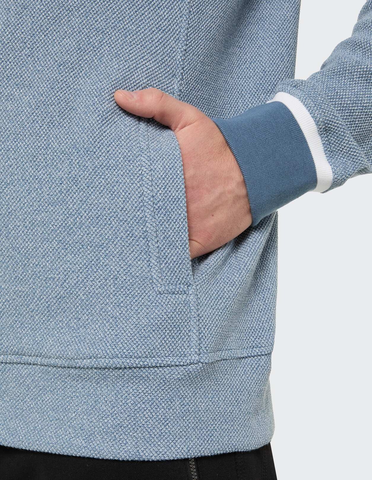 Nahaufnahme eines blauen, strukturierten Sweatshirts mit einer Hand in der Tasche.