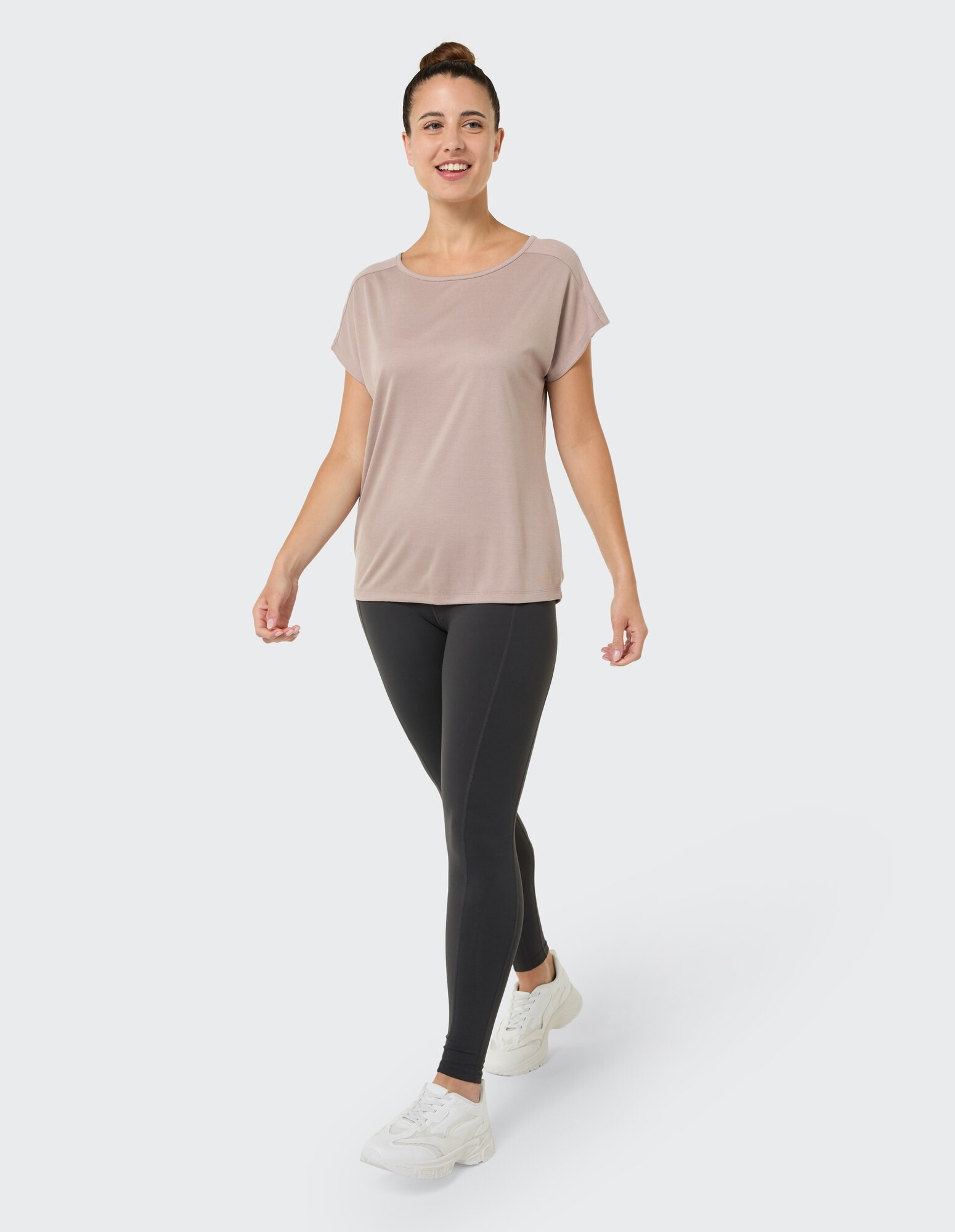 Frau in einem hellbraunen, locker sitzenden Oberteil und schwarzen Leggings geht lässig spazieren.