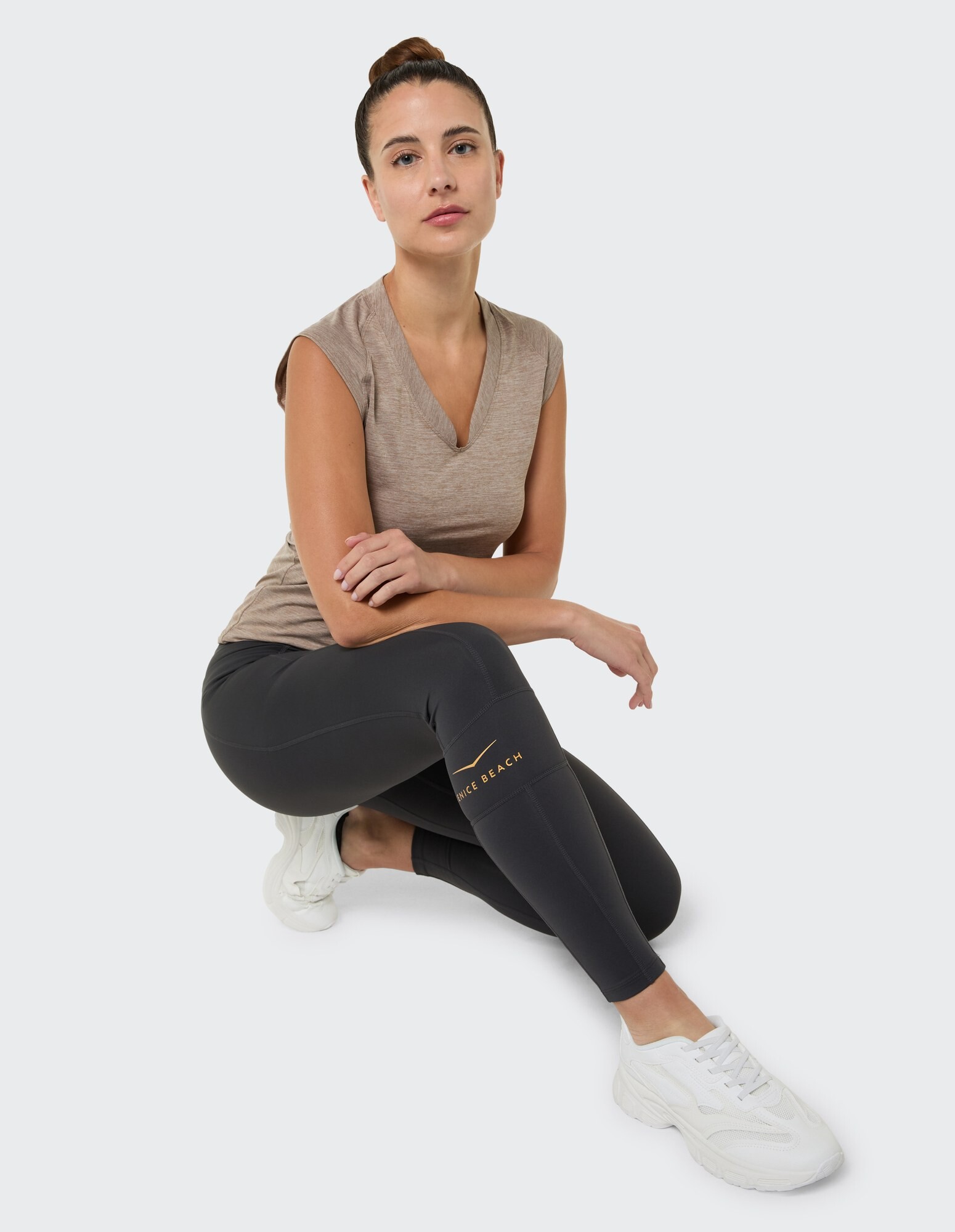 Frau in einem braunen Top mit V-Ausschnitt und schwarzen Leggings, gestylt für lässigen Komfort.