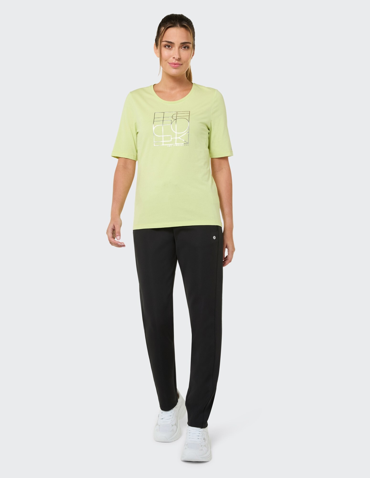 Frau in einem hellgrünen Grafik-T-Shirt und einer schwarzen Hose, gestylt für Freizeitkleidung.