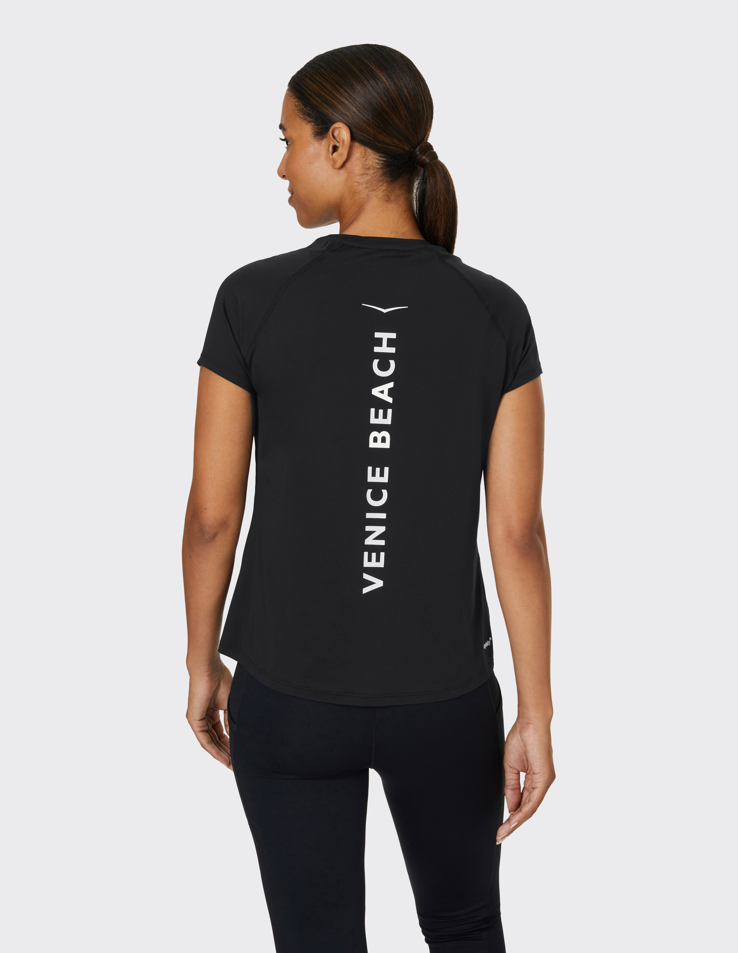 Frau trägt ein schwarzes lässiges T-Shirt von Venice Beach mit Logo-Aufdruck auf der Rückseite.