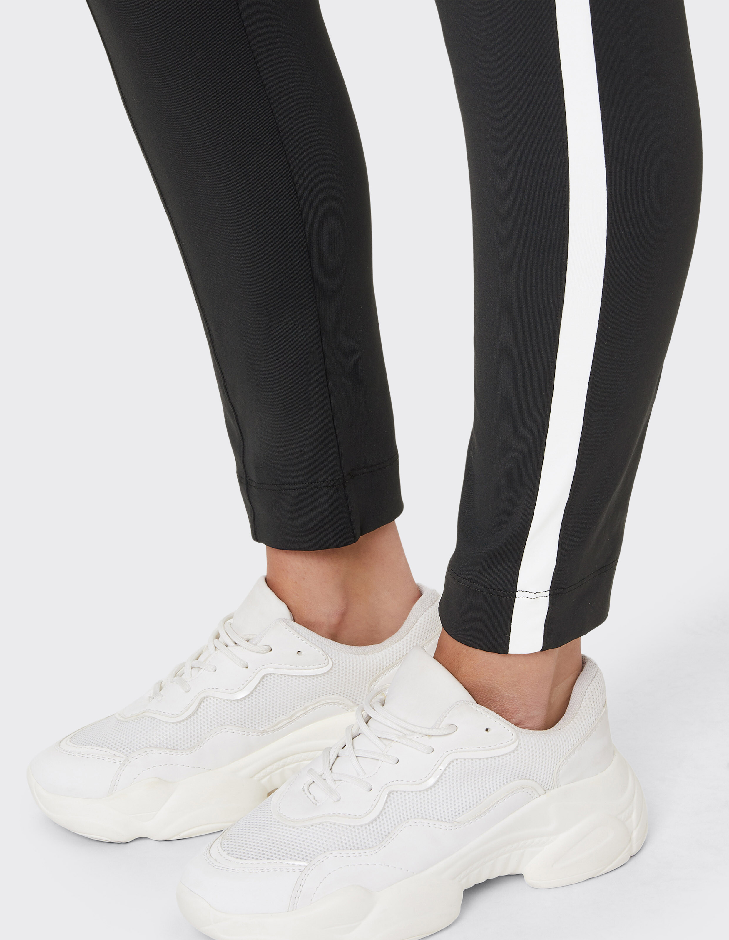 Nahaufnahme von schwarzen Leggings mit weißen Streifen und stylischen weißen Sneakers.