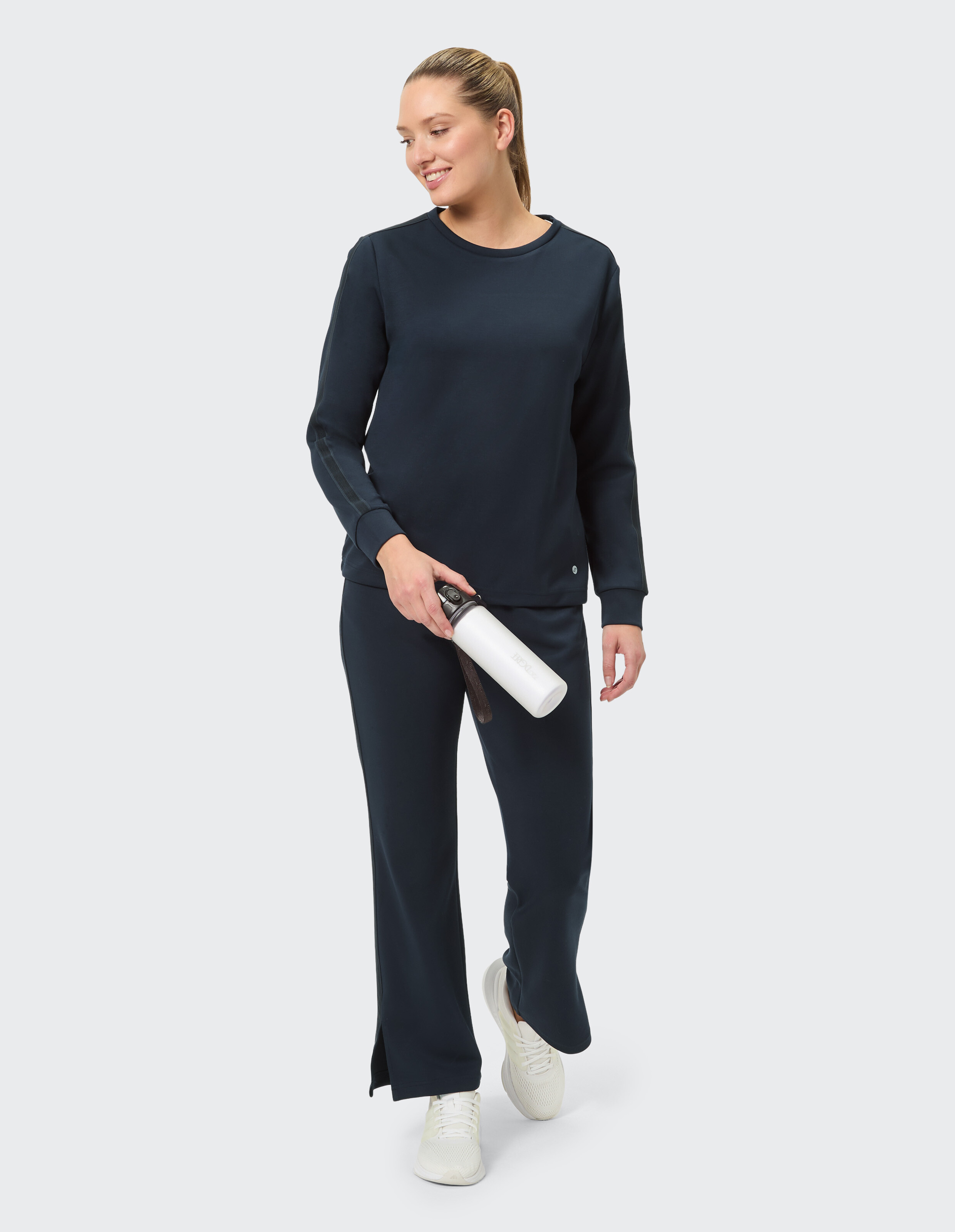 Frau in dunkelblauer Freizeitkleidung, bestehend aus einem langärmligen Oberteil und einer Hose mit weitem Bein, perfekt zum Faulenzen oder für Freizeitausflüge.