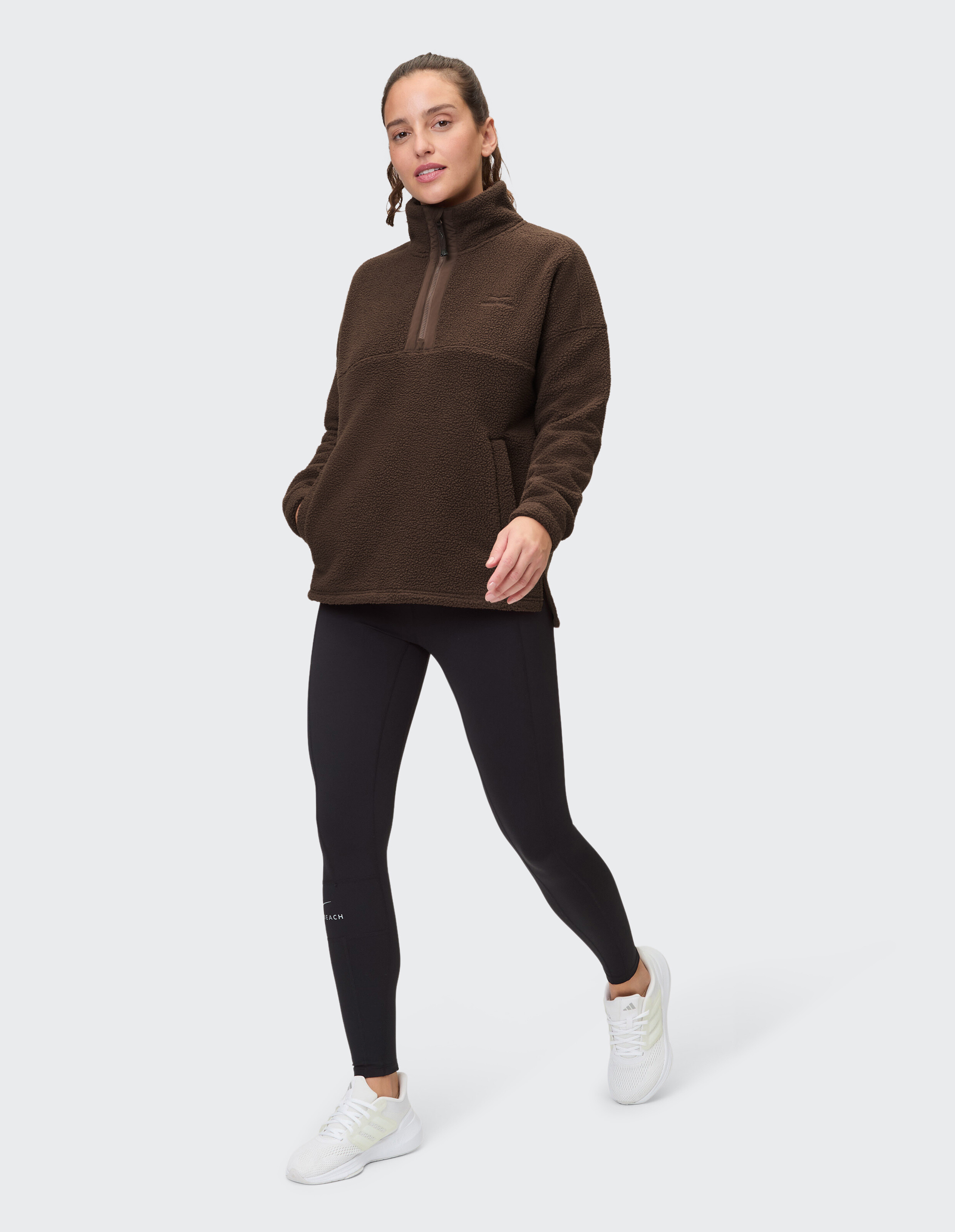 Frau trägt einen braunen Fleece-Pullover mit halbem Reißverschluss und schwarze Leggings für lässigen Komfort.