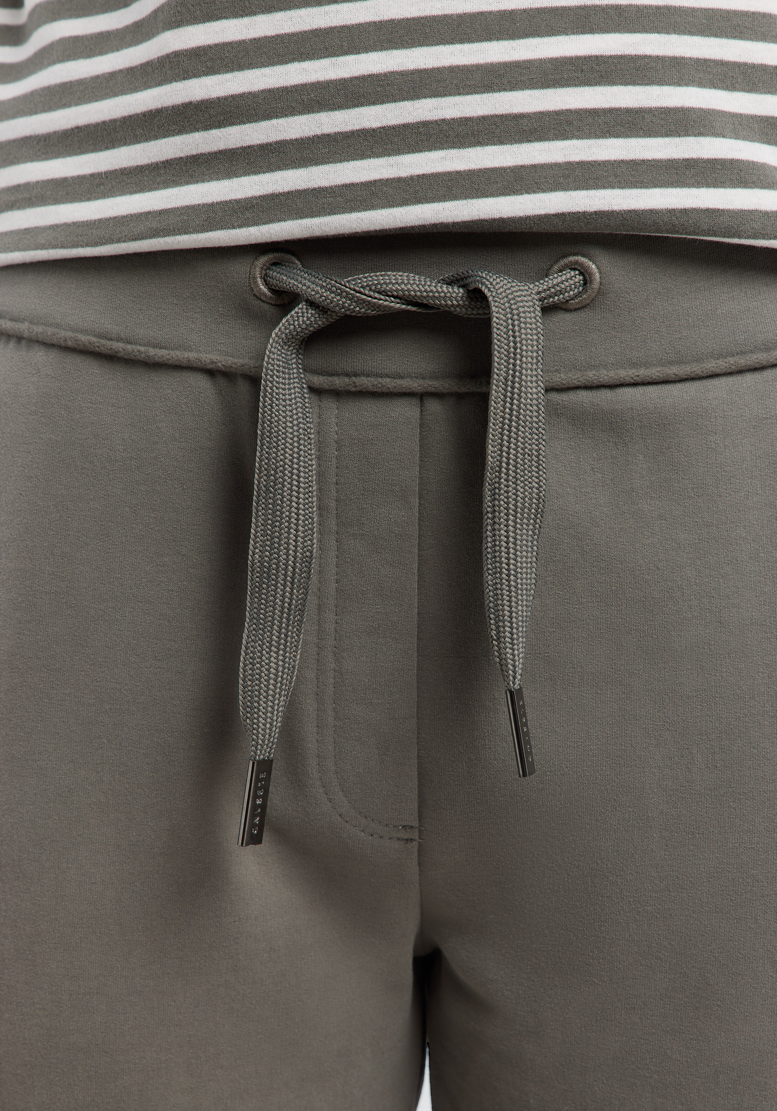 Nahaufnahme einer olivgrünen Jogginghose mit Kordelzug in der Taille und gestreiftem Oberteil.
