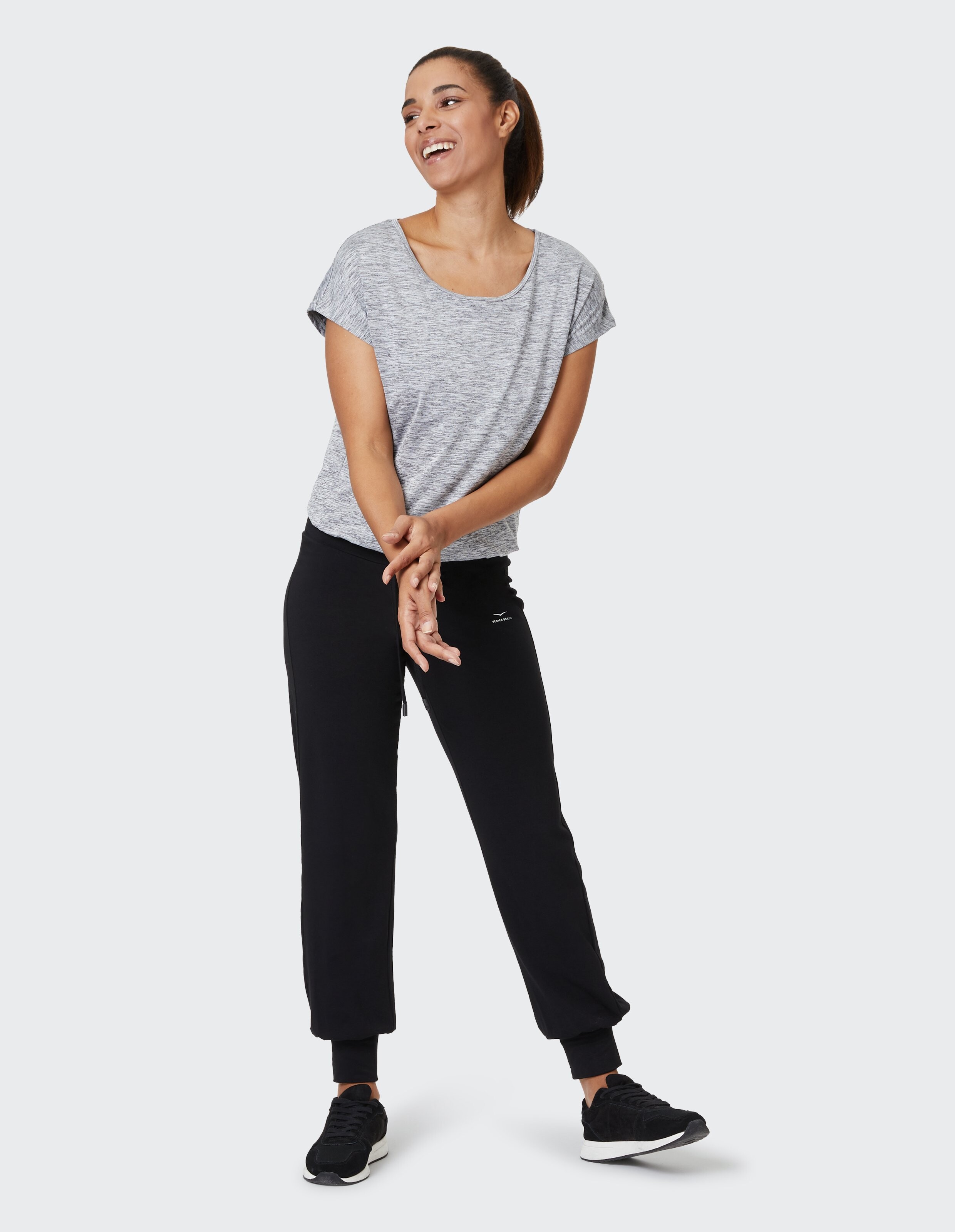 Frau trägt ein grau meliertes T-Shirt und schwarze Jogginghosen für einen gemütlichen, lässigen Lounge-Look.