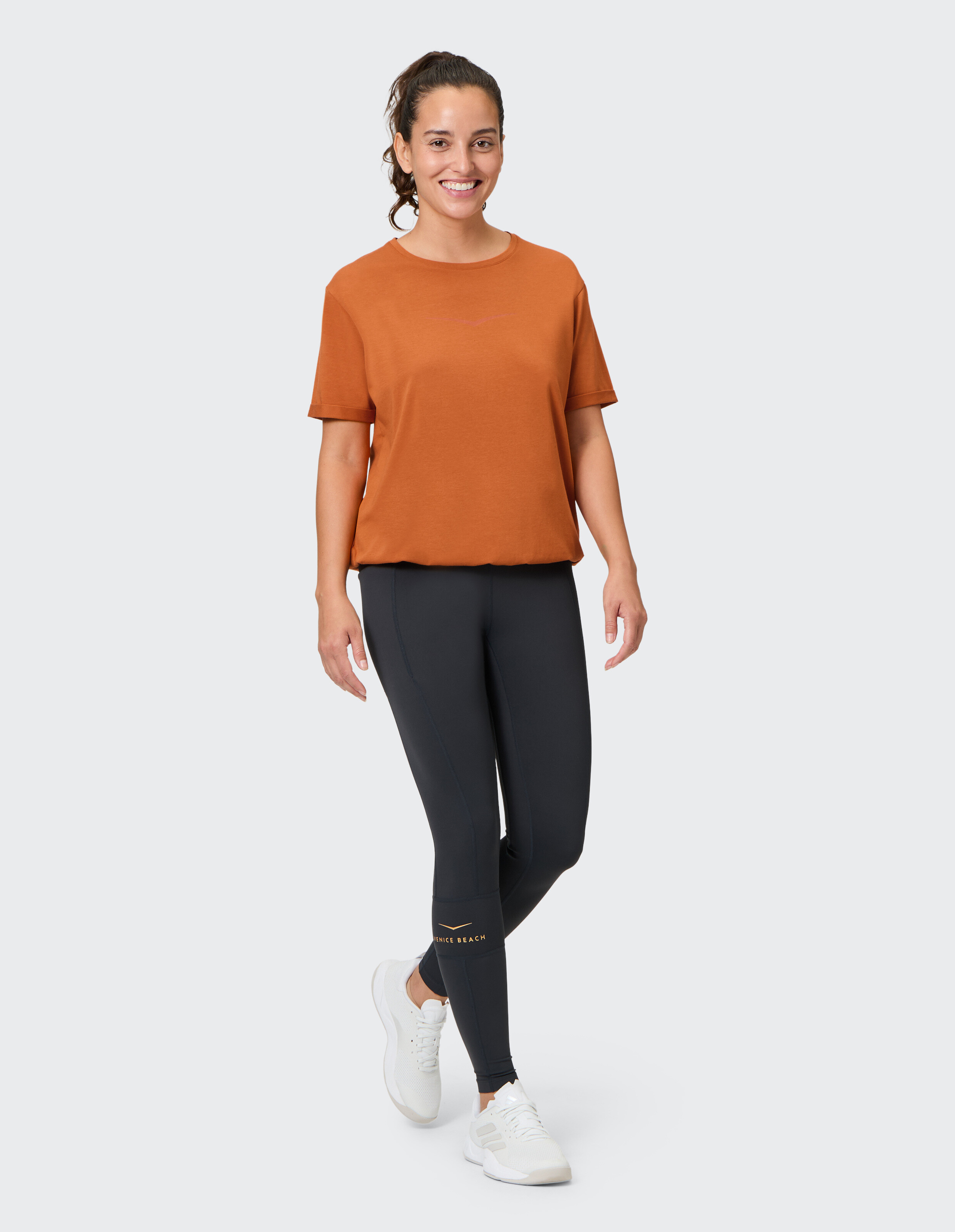 Frau in einem orangefarbenen T-Shirt und schwarzen Leggings, die einen lässigen Activewear-Stil präsentiert.