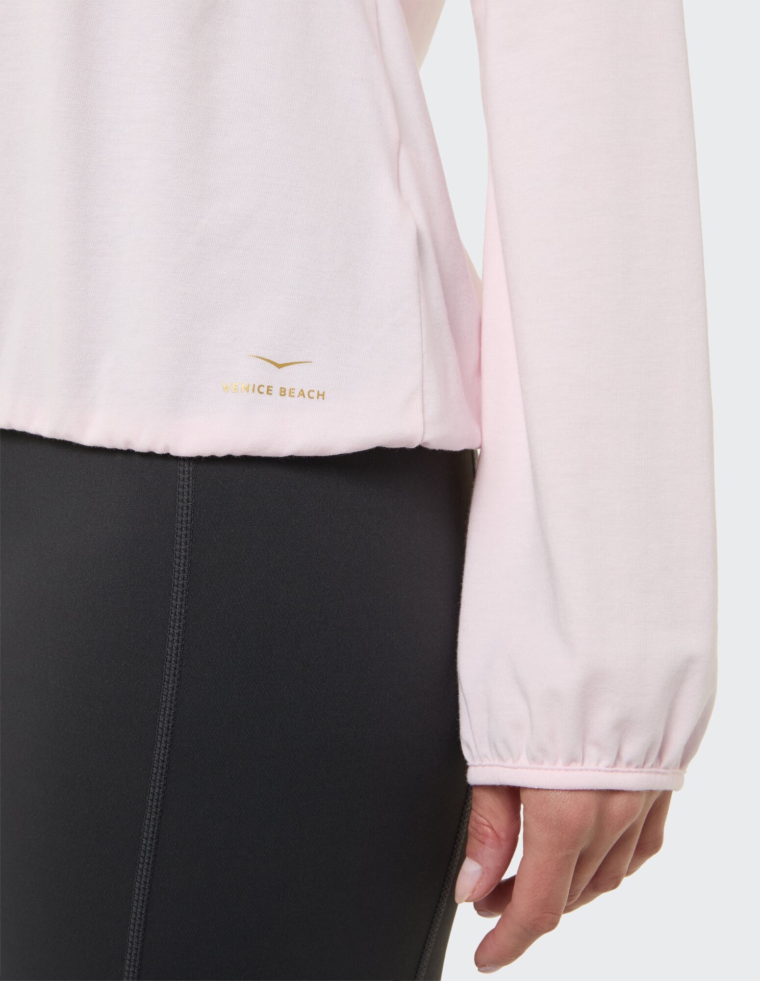 Nahaufnahme eines hellrosa Langarmoberteils mit gerafften Bündchen und Logodetail.