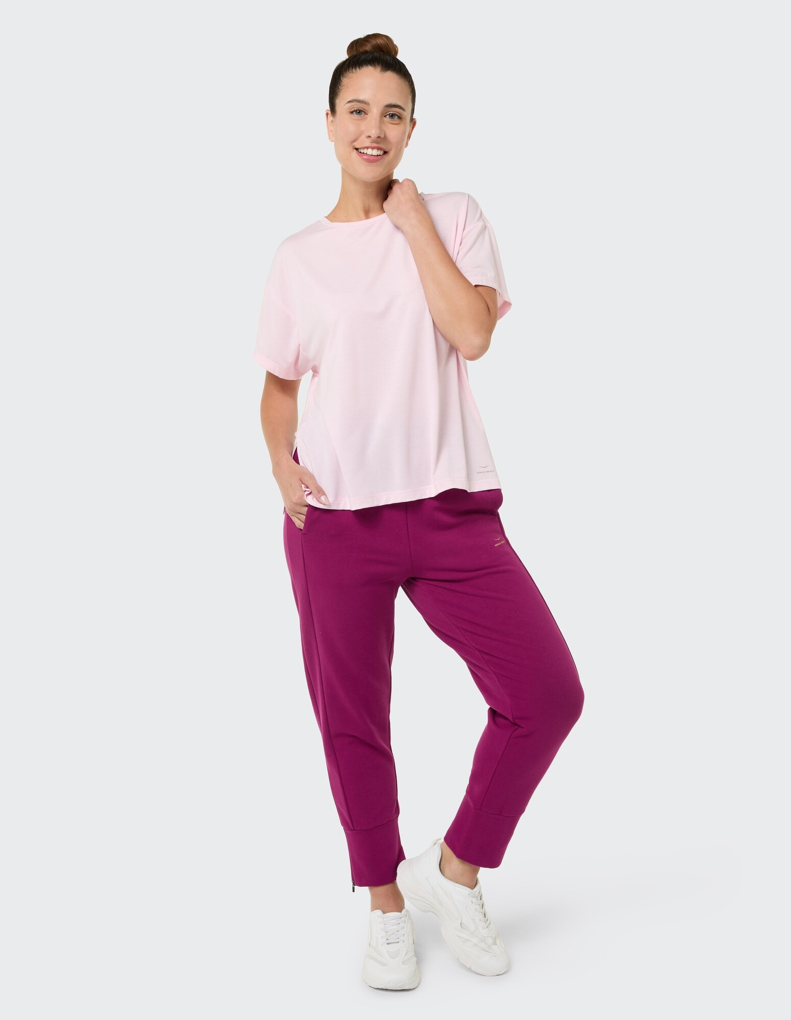 Frau in rosa T-Shirt und lila Jogginghose präsentiert lässige, bequeme Kleidung.