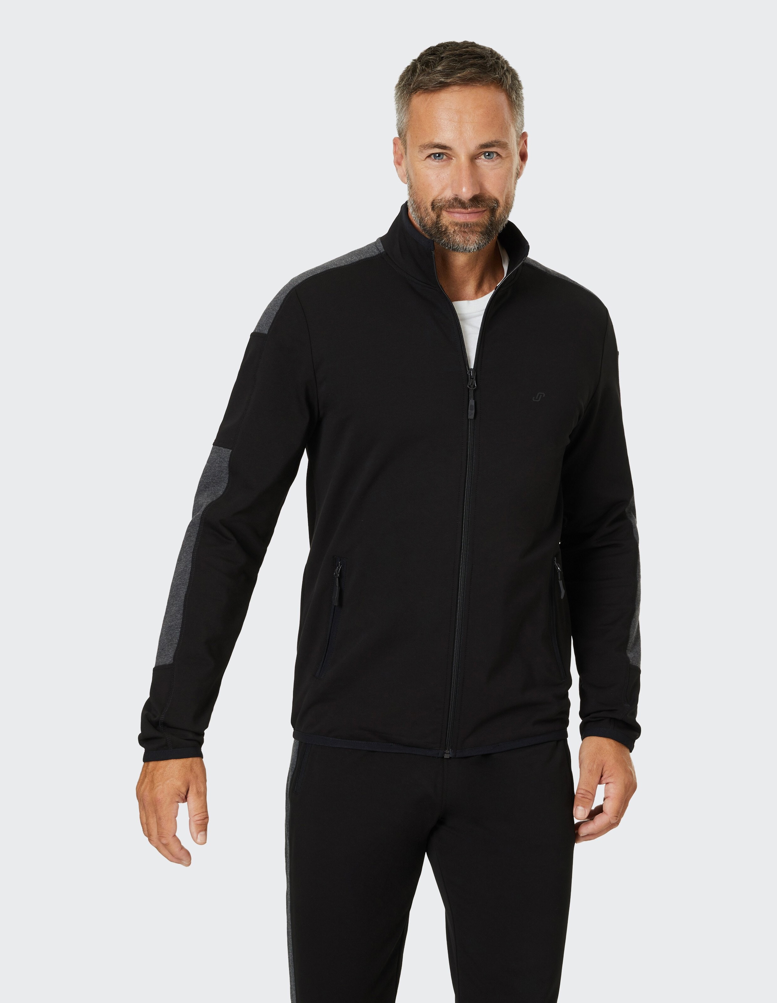 Schwarze Jacke mit grauen Ärmeln, durchgehendem Reißverschluss, Stehkragen und seitlichen Reißverschlusstaschen.