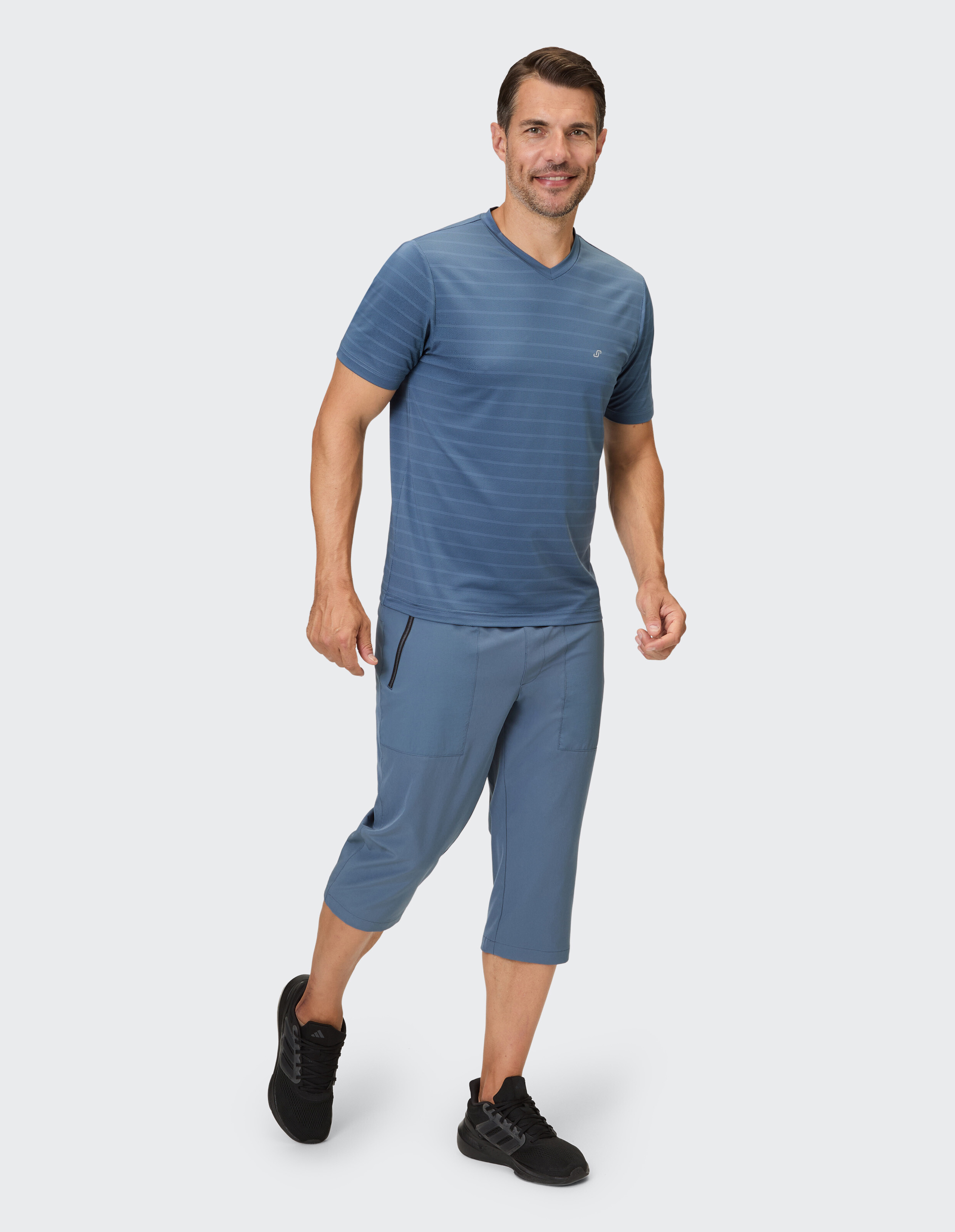 Mann in einem blau gestreiften T-Shirt mit V-Ausschnitt und einer kurzen Hose, gestylt für Freizeitkleidung.