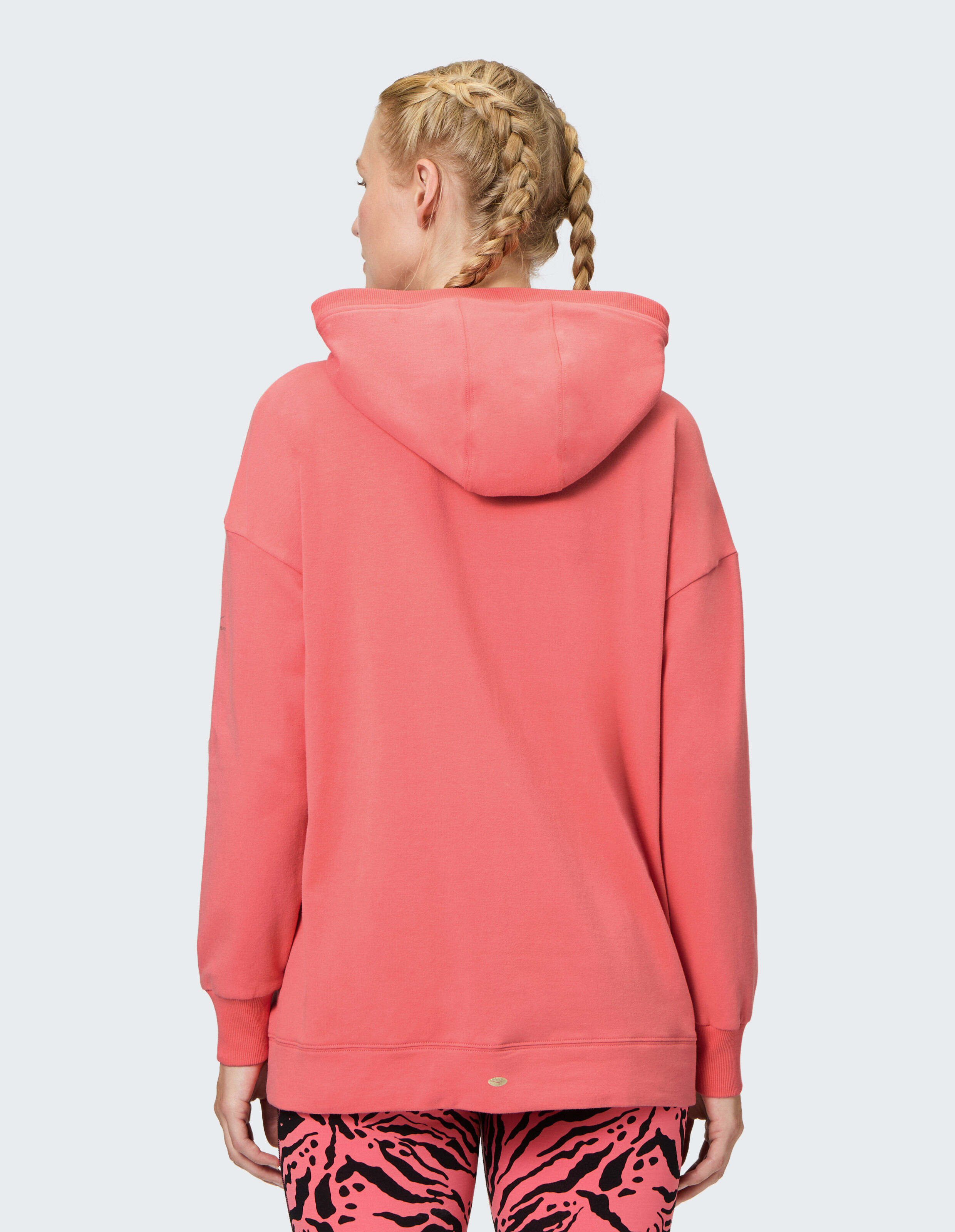 Rückansicht einer Frau in einem korallenroten Kapuzenpullover gepaart mit rosa Leggings mit Zebramuster.