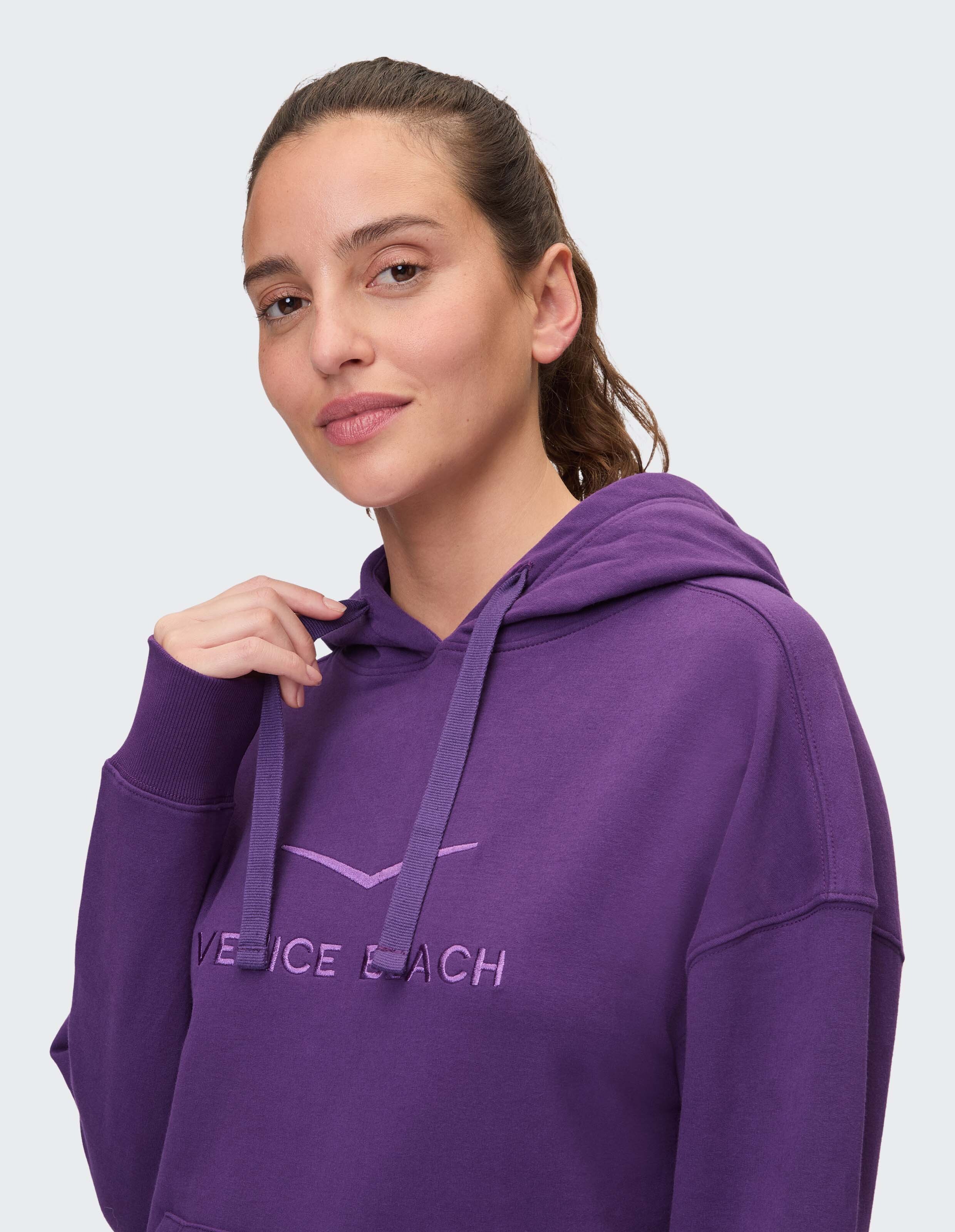 Frau trägt einen lila Kapuzenpullover mit „Venice Beach“-Stickerei und unterstreicht damit den lässigen Stil.