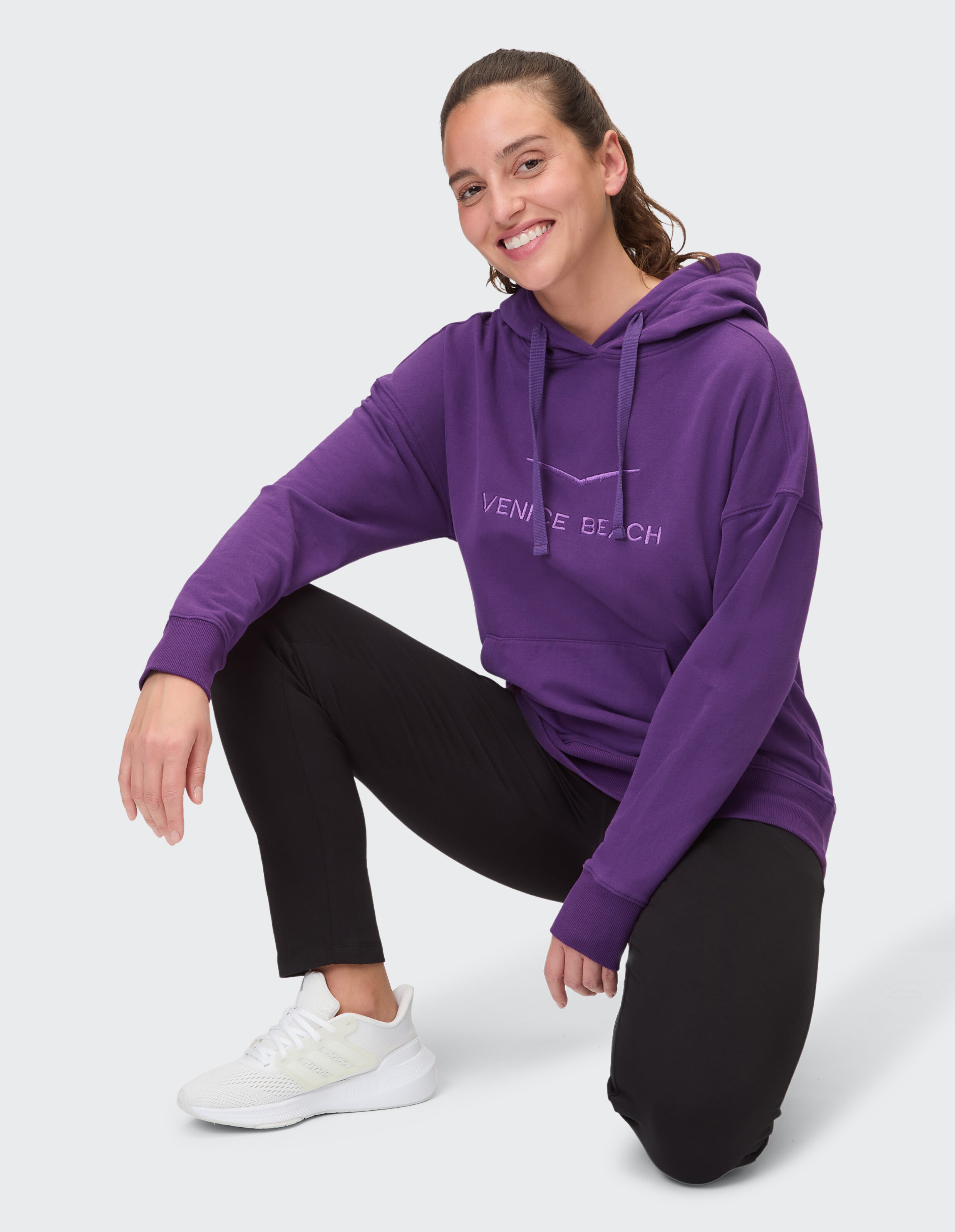 Frau trägt einen gemütlichen lilafarbenen Venice Beach-Hoodie und schwarze Leggings für Freizeitkleidung.